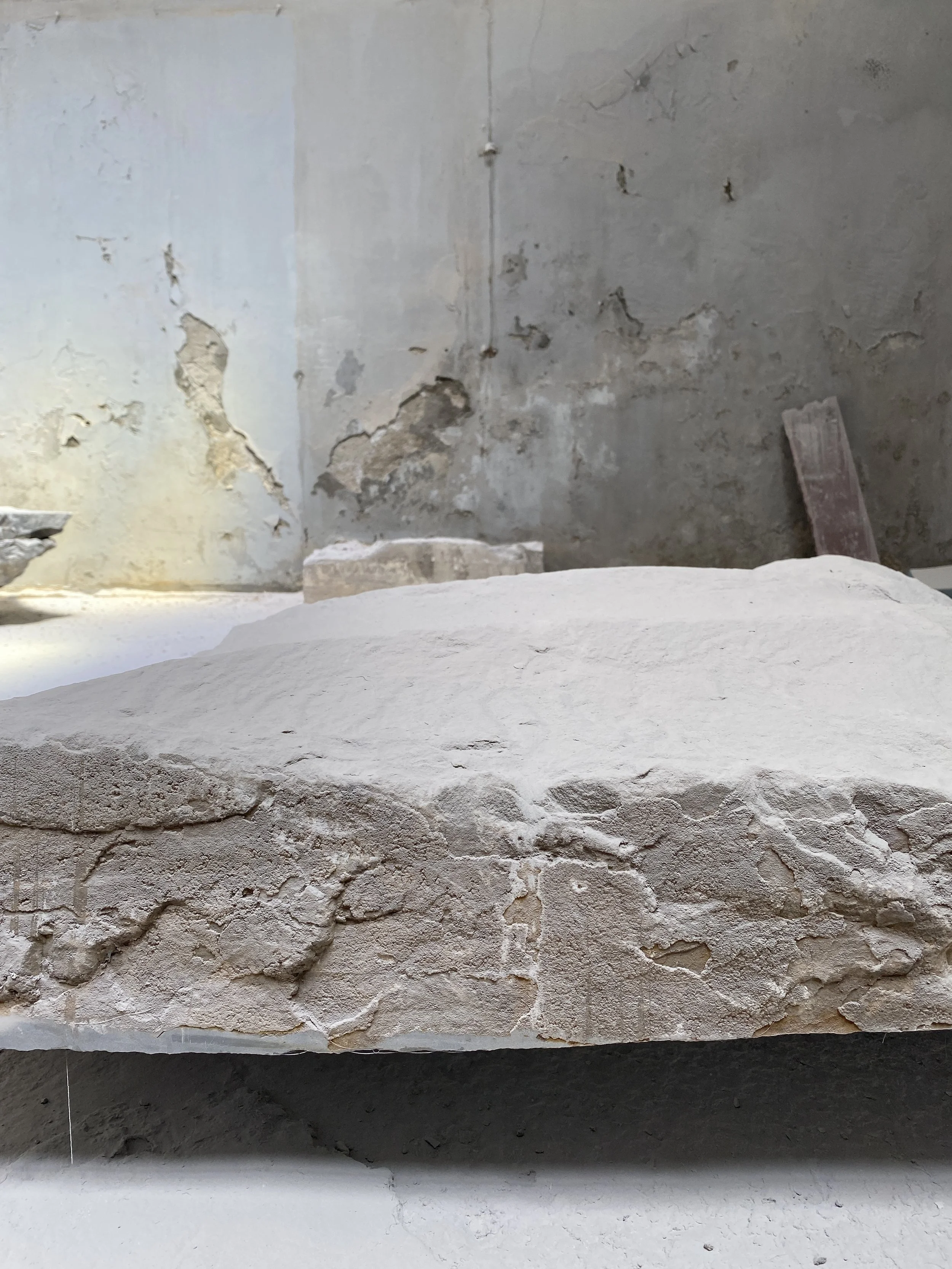 Close-up of a large, textured stone block in a room with peeling and cracked walls.