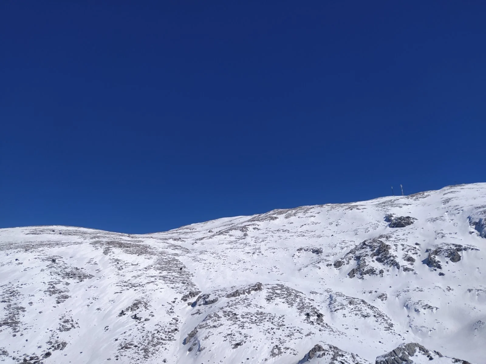 Snow-covered mountain slope with rocky patches under a clear blue sky.