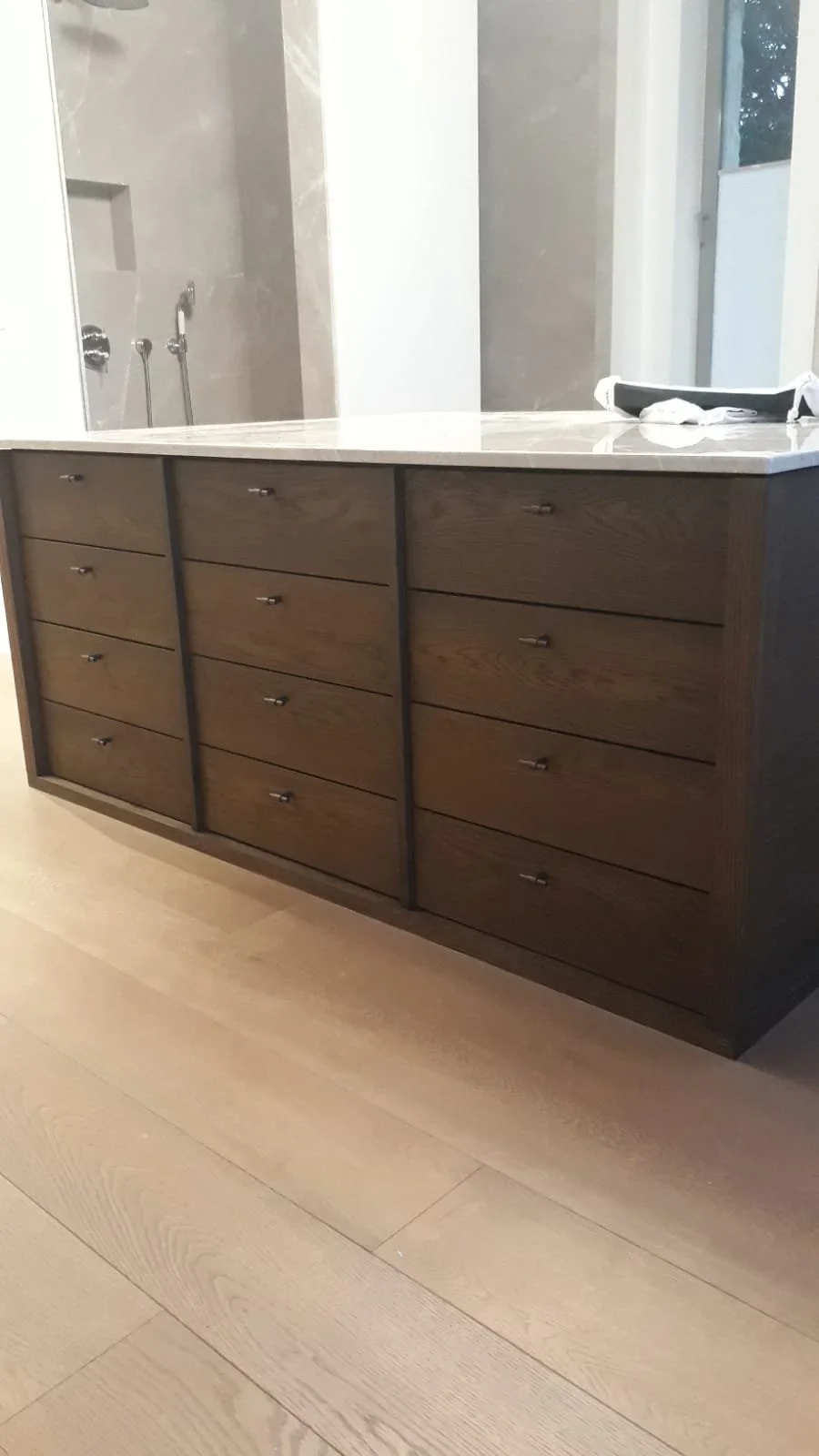 A modern bathroom vanity with a marble countertop and multiple wooden drawers, set against a light-colored wall with a mirror above.