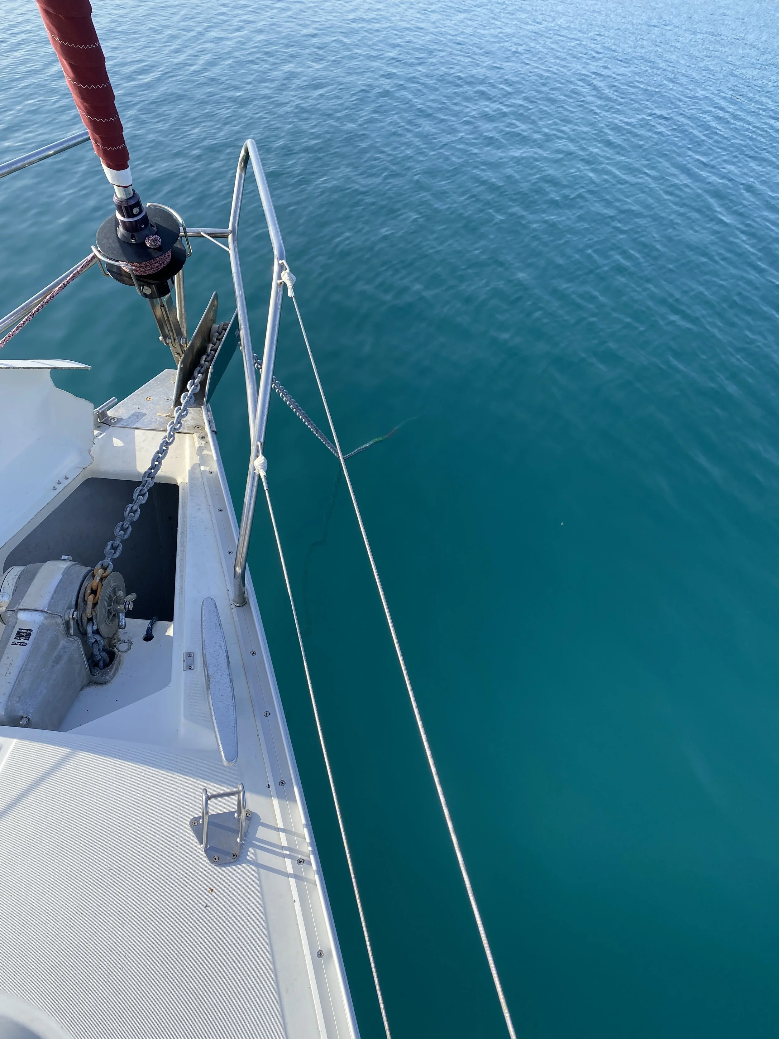 View of the front section of a sailboat with taut rigging and a red sail cover, floating on calm blue water.