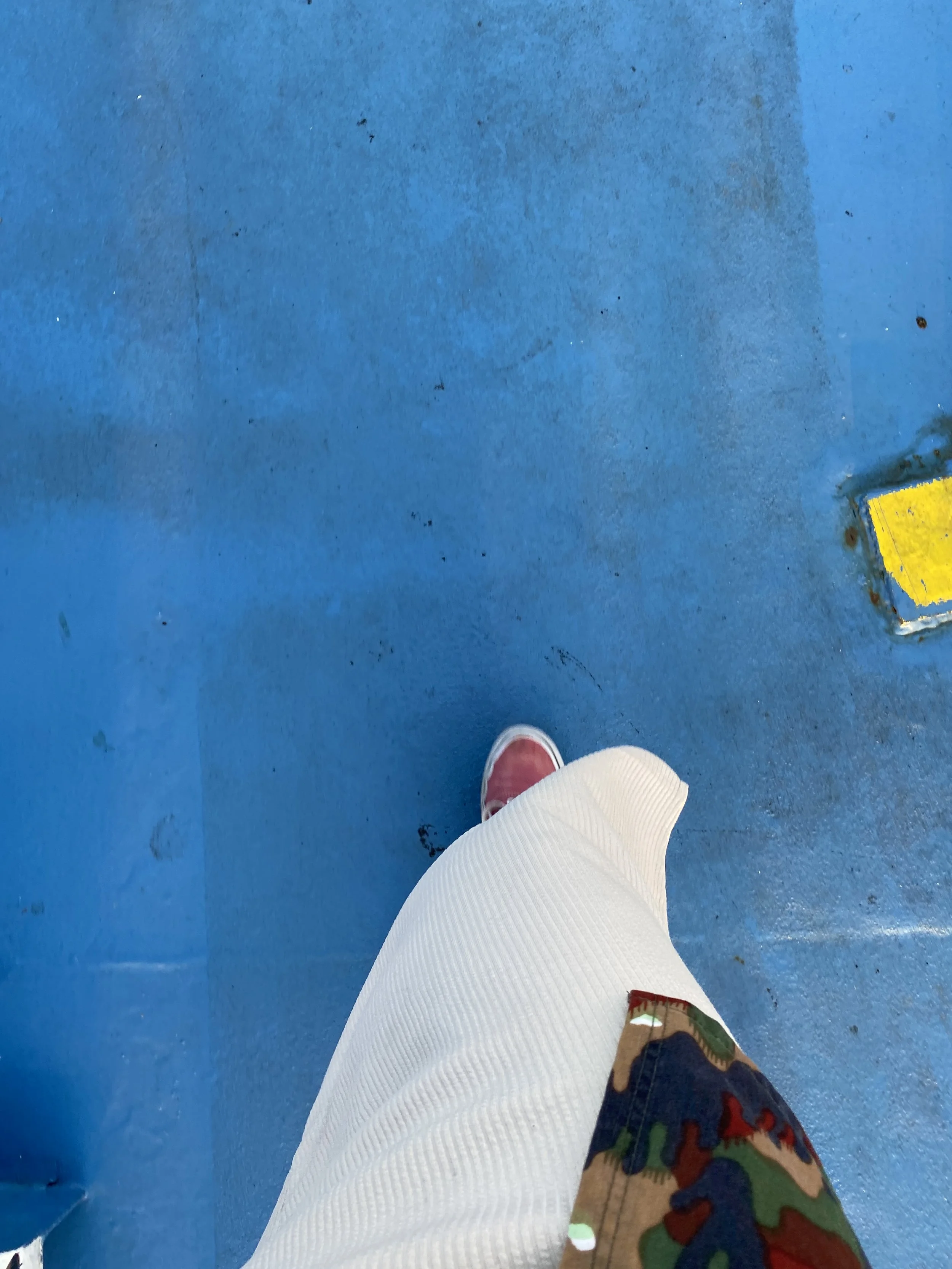 A person wearing red shoes and a white skirt, standing on a blue floor near a yellow object.