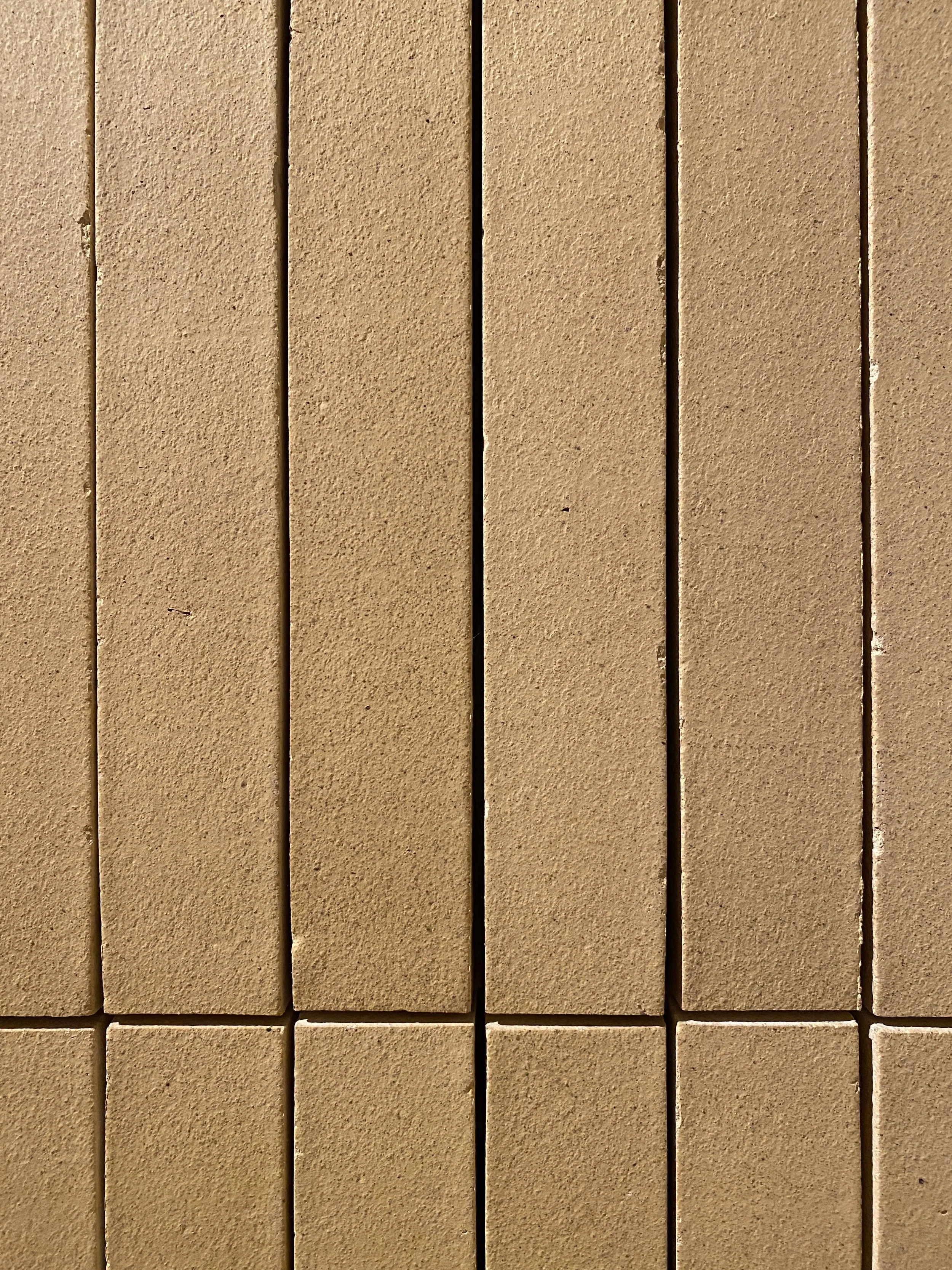 Close-up of beige textured brick wall with vertical and horizontal seams.
