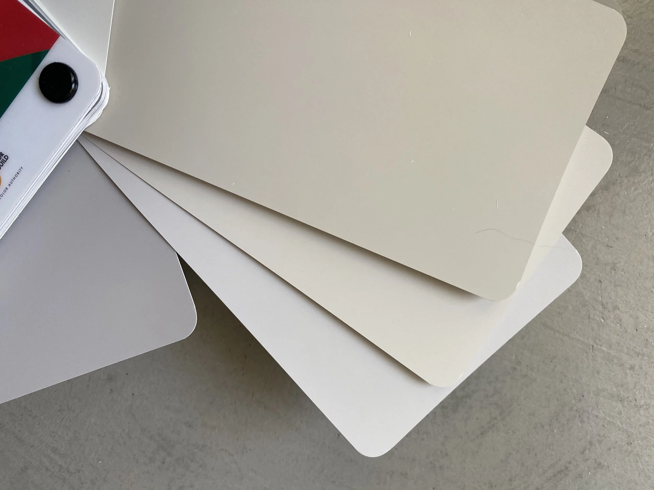Sample color swatches in neutral shades of beige, off-white, and light gray, arranged on a surface.
