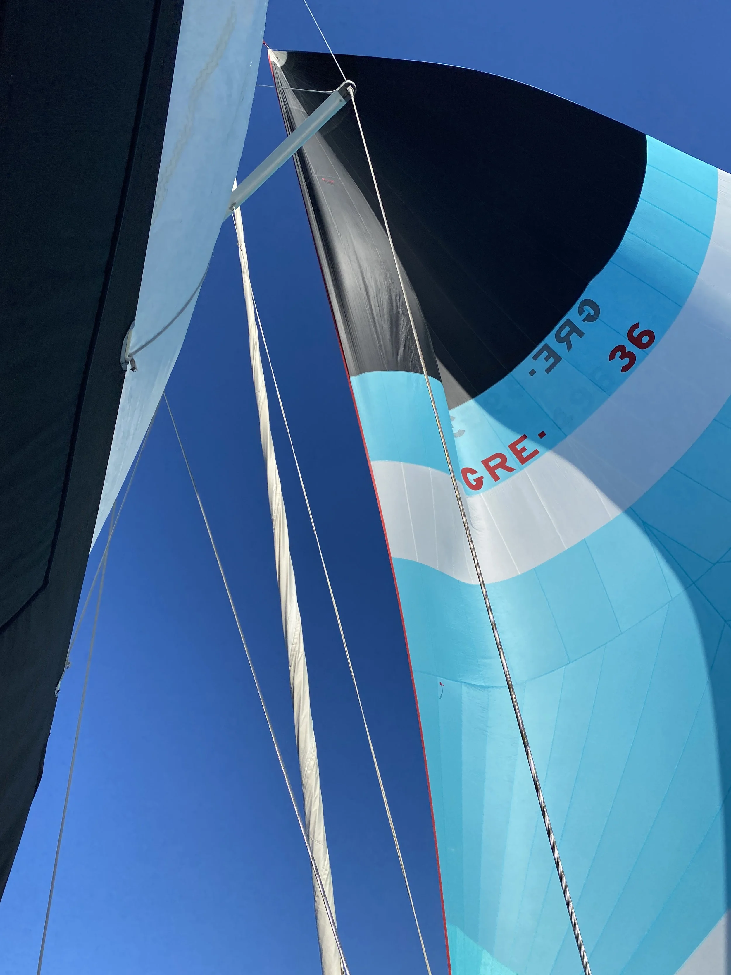 Sailboats with colorful sails on blue sky, seen from below.