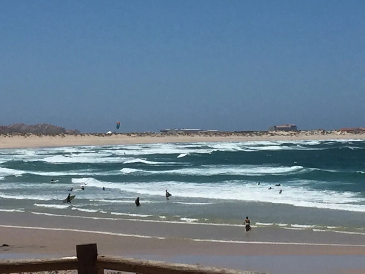 People surfing and swimming at the beach with waves and a sandy shoreline under a clear sky.