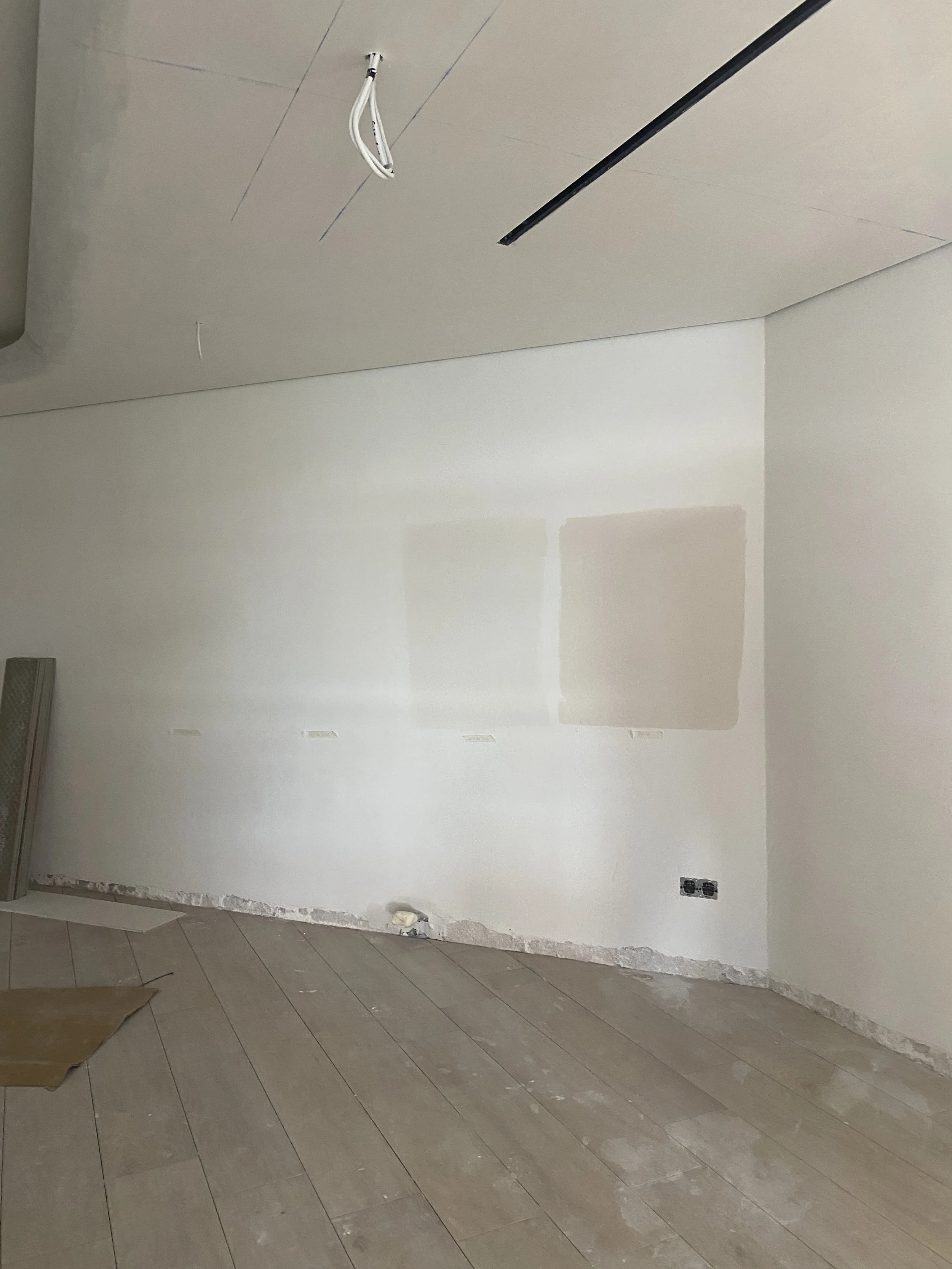 Unfinished interior room with drywall on the walls, electrical outlets installed, and the ceiling partially under construction with hanging wires and mounting tracks.
