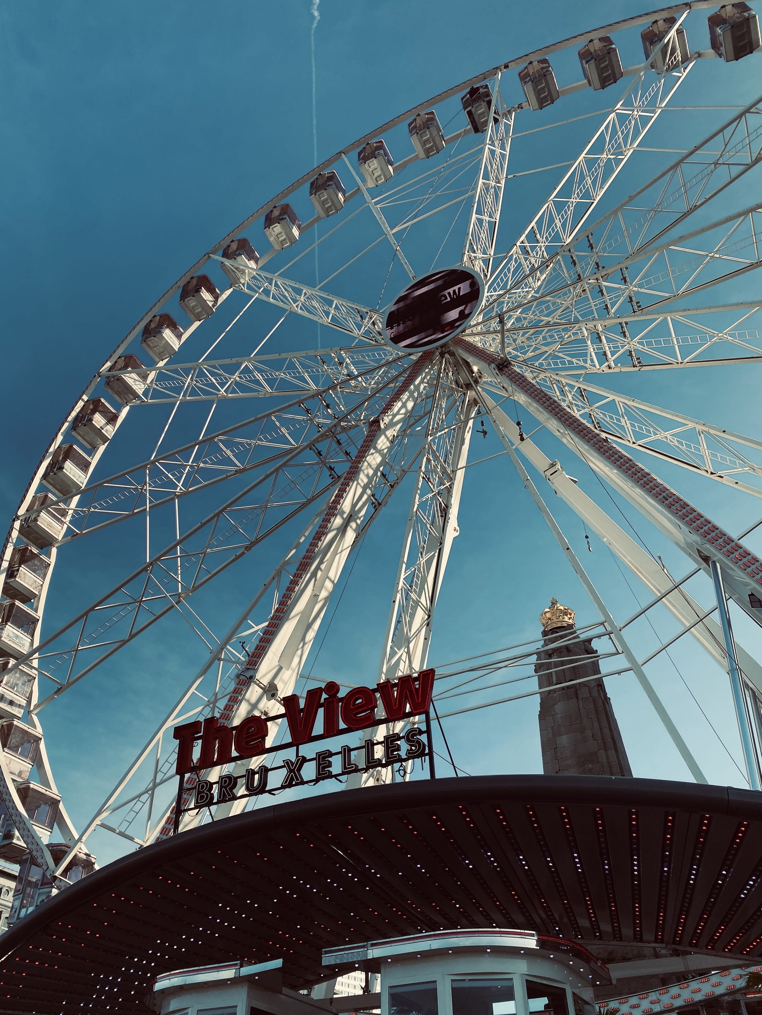 A large Ferris wheel with enclosed cabins against a clear blue sky, with a sign reading 'The View Brussels' below it.