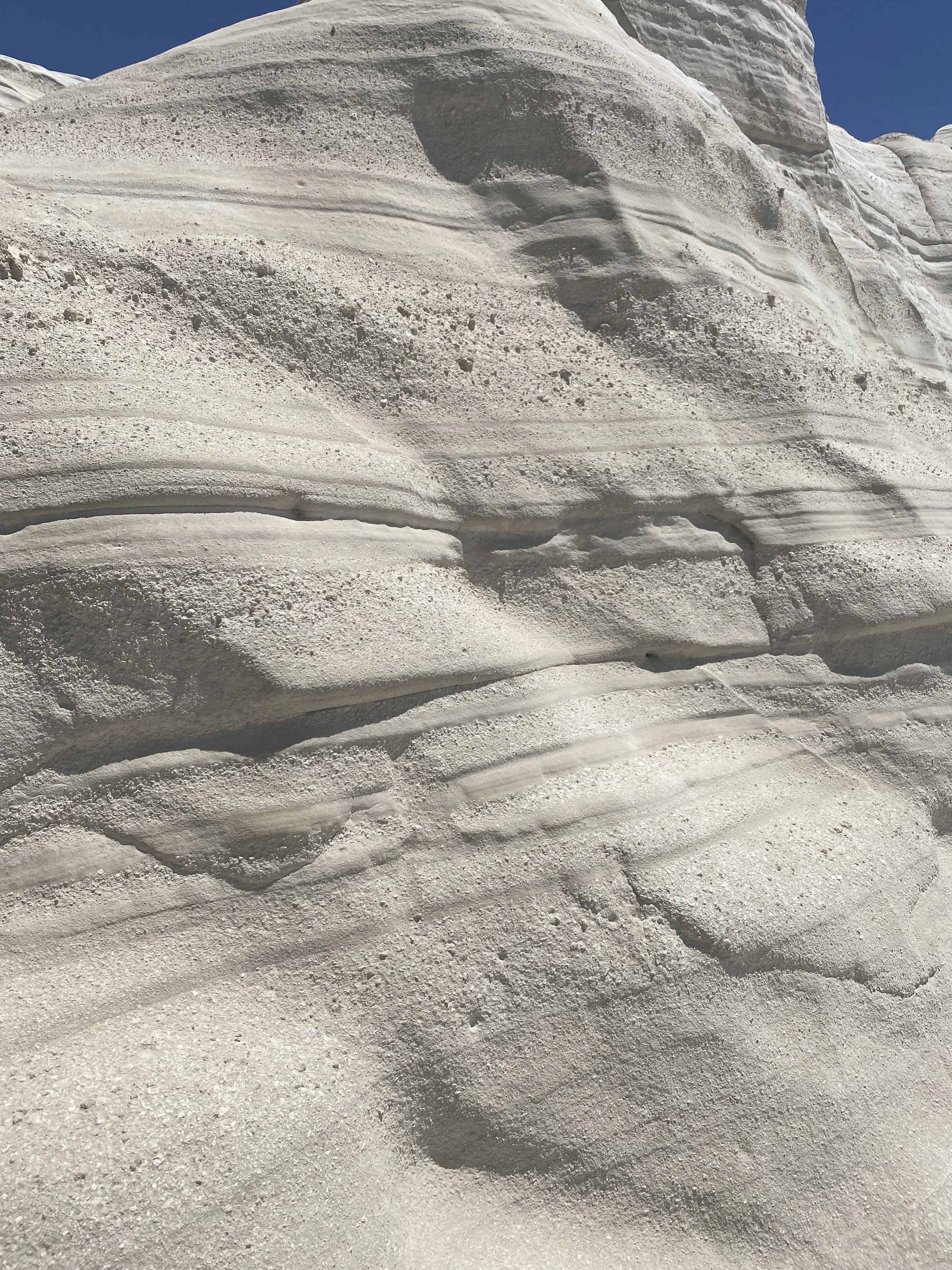 Close-up of layered white and gray sandstone rock formations with a clear blue sky in the background.