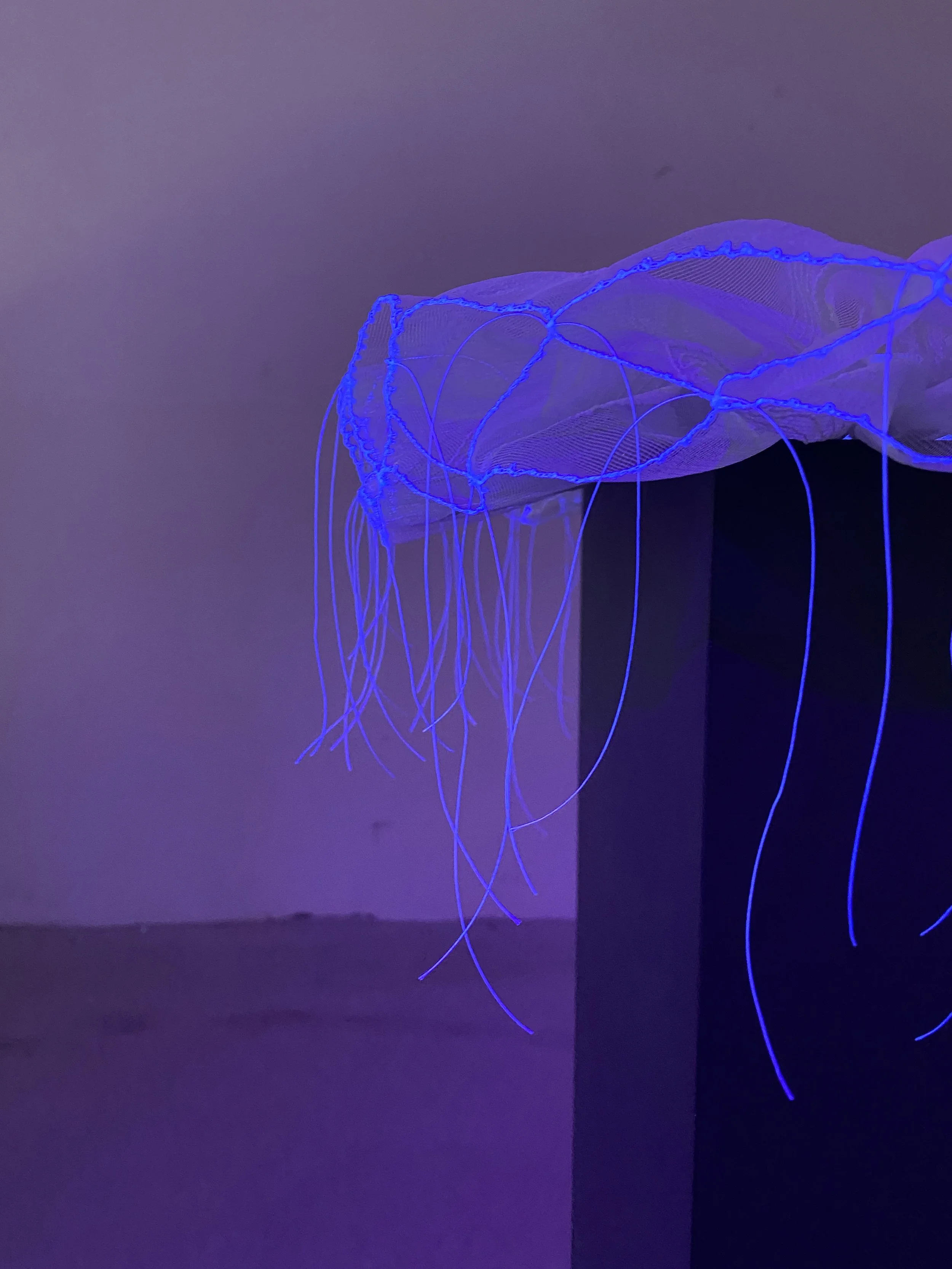 Abstract artwork with glowing blue threads hanging from a mesh fabric, illuminated under black light.