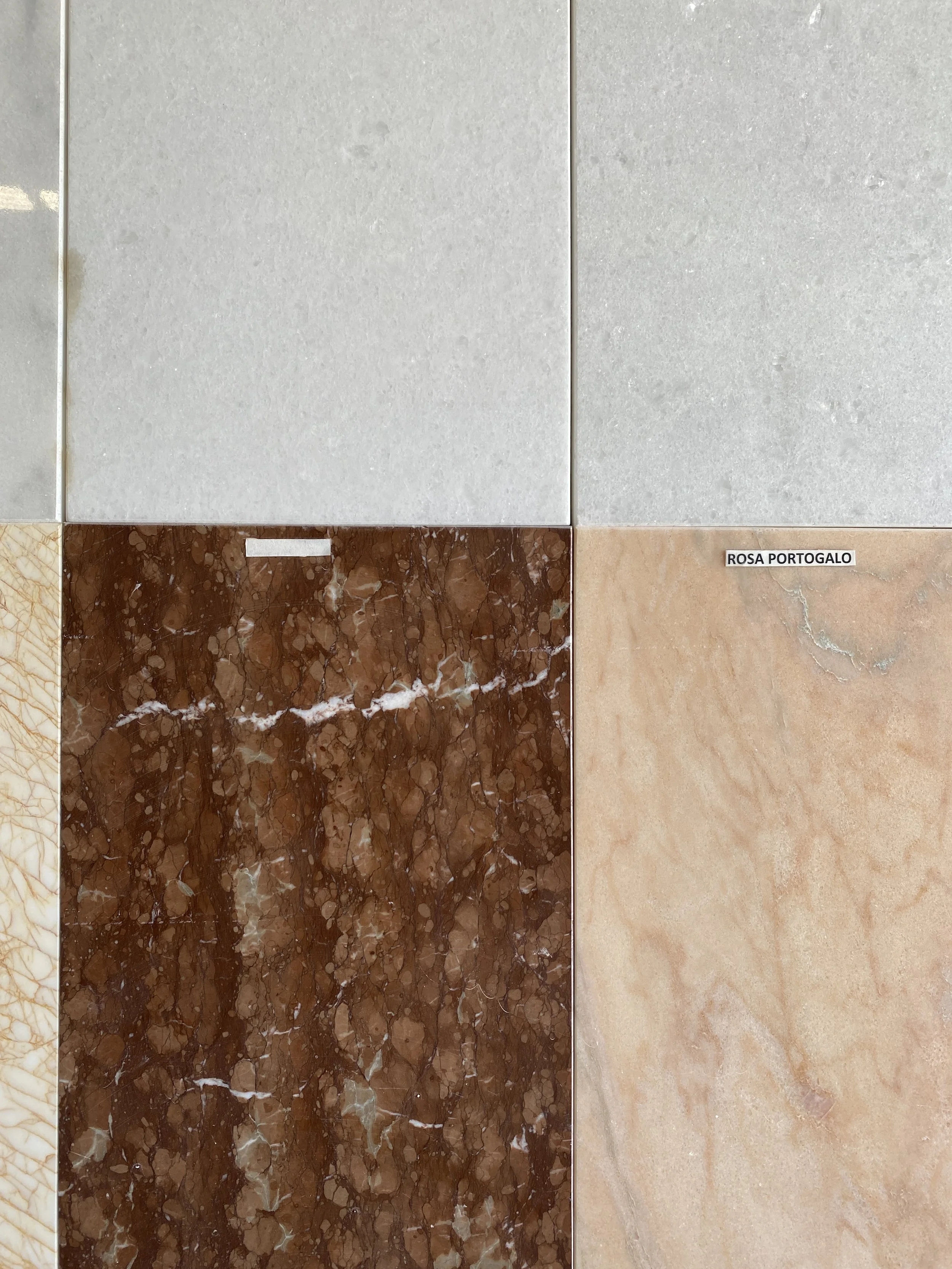 Collection of ceramic tiles with various textures and colors, including cream, gray, brown marble, and beige with a label reading 'ROSA PORTUGALO'.