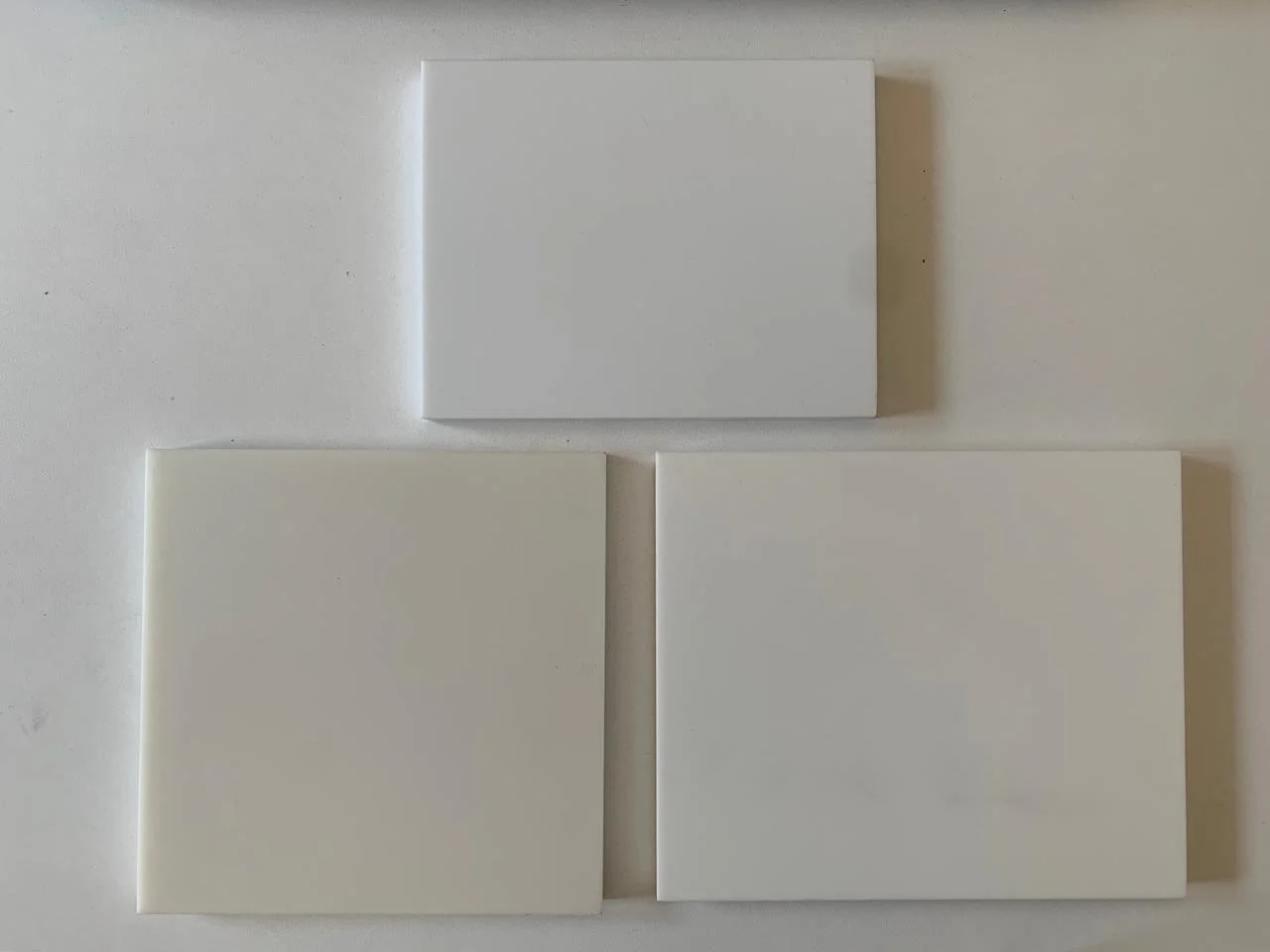 Three plain white tiles arranged on a wall, two at the bottom and one at the top.