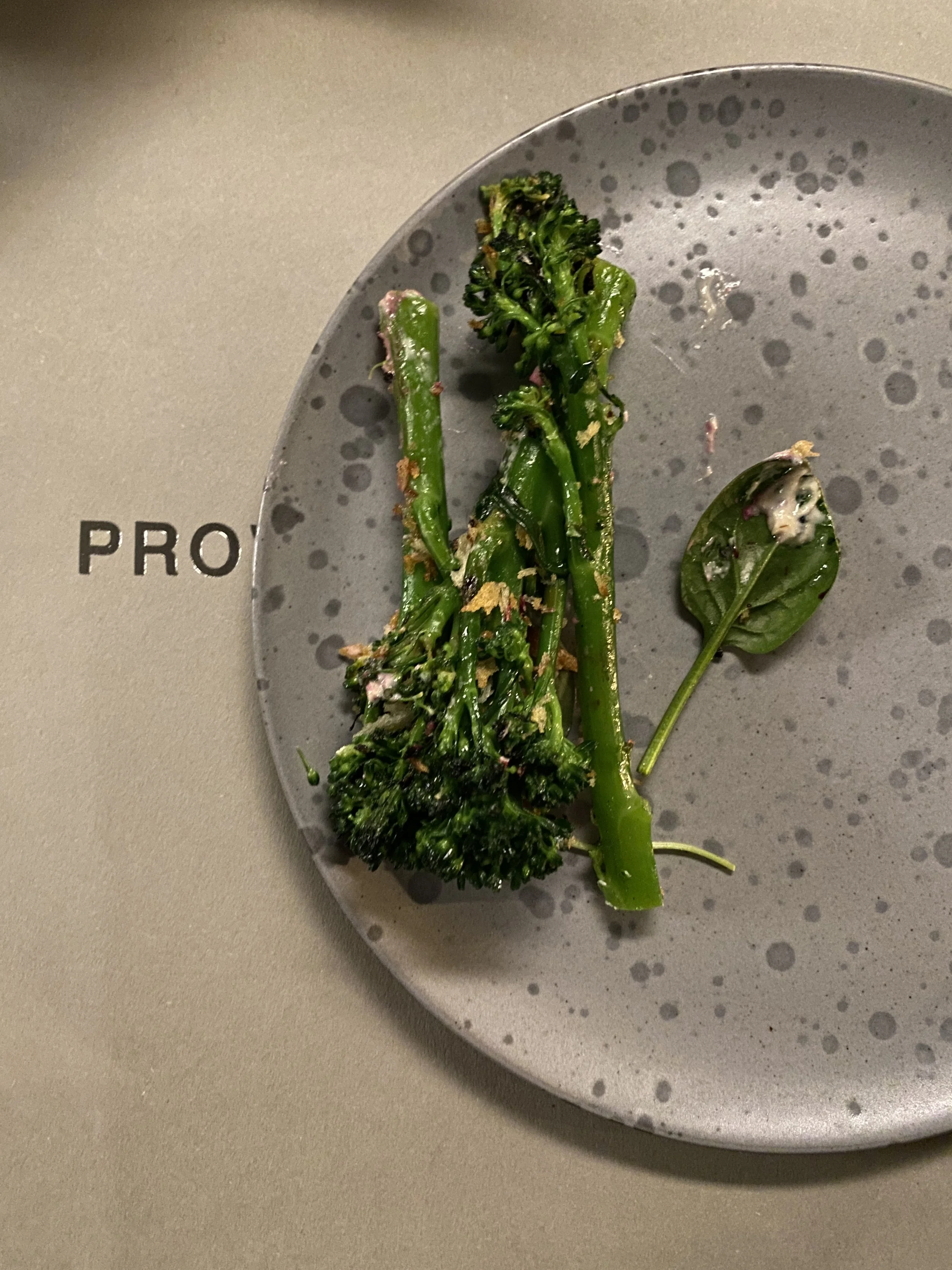 Cooked green broccoli, spinach, and herbs on a speckled gray plate.