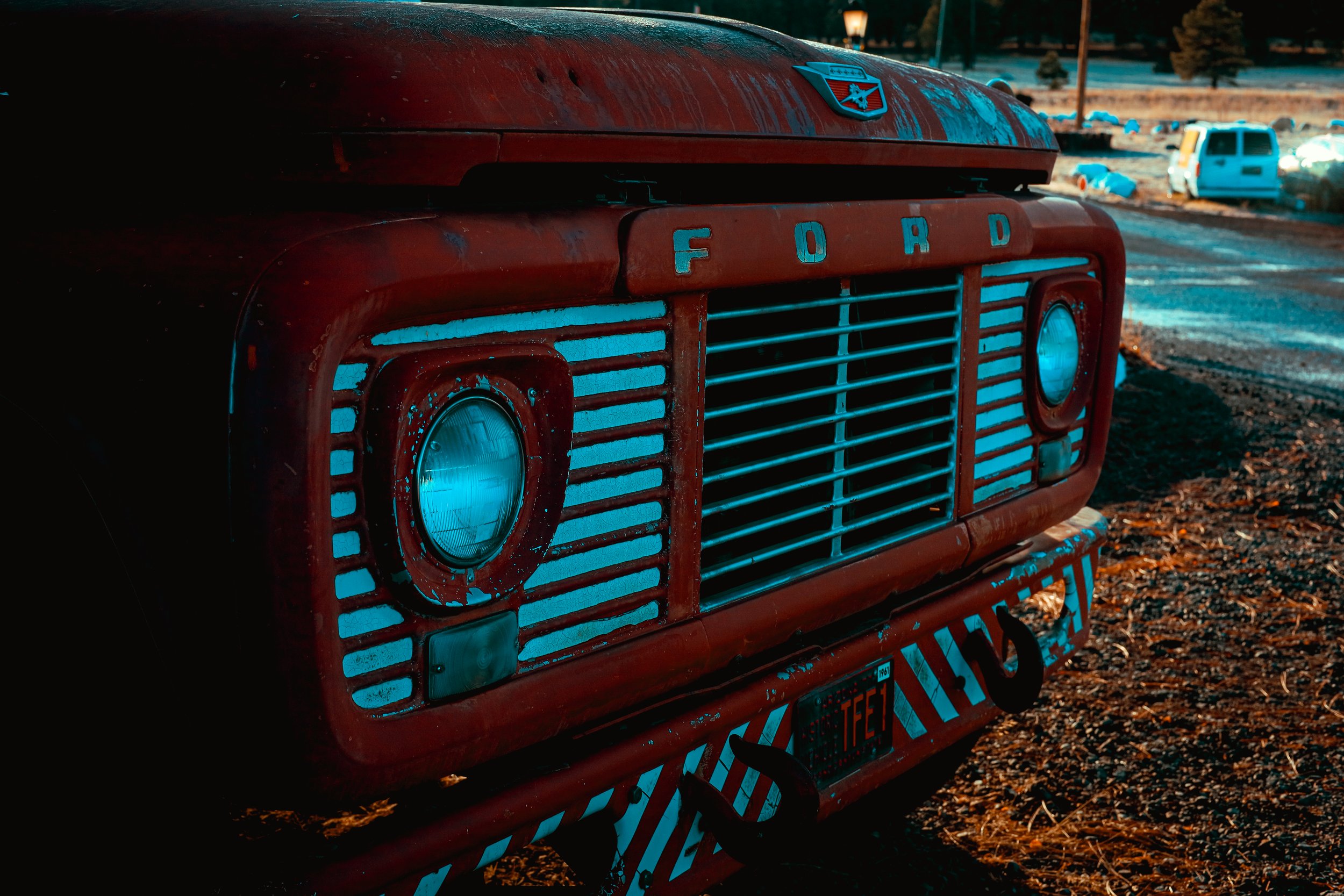 Close-up of a vintage red Ford truck grille with round headlights and a rusty, weathered appearance.