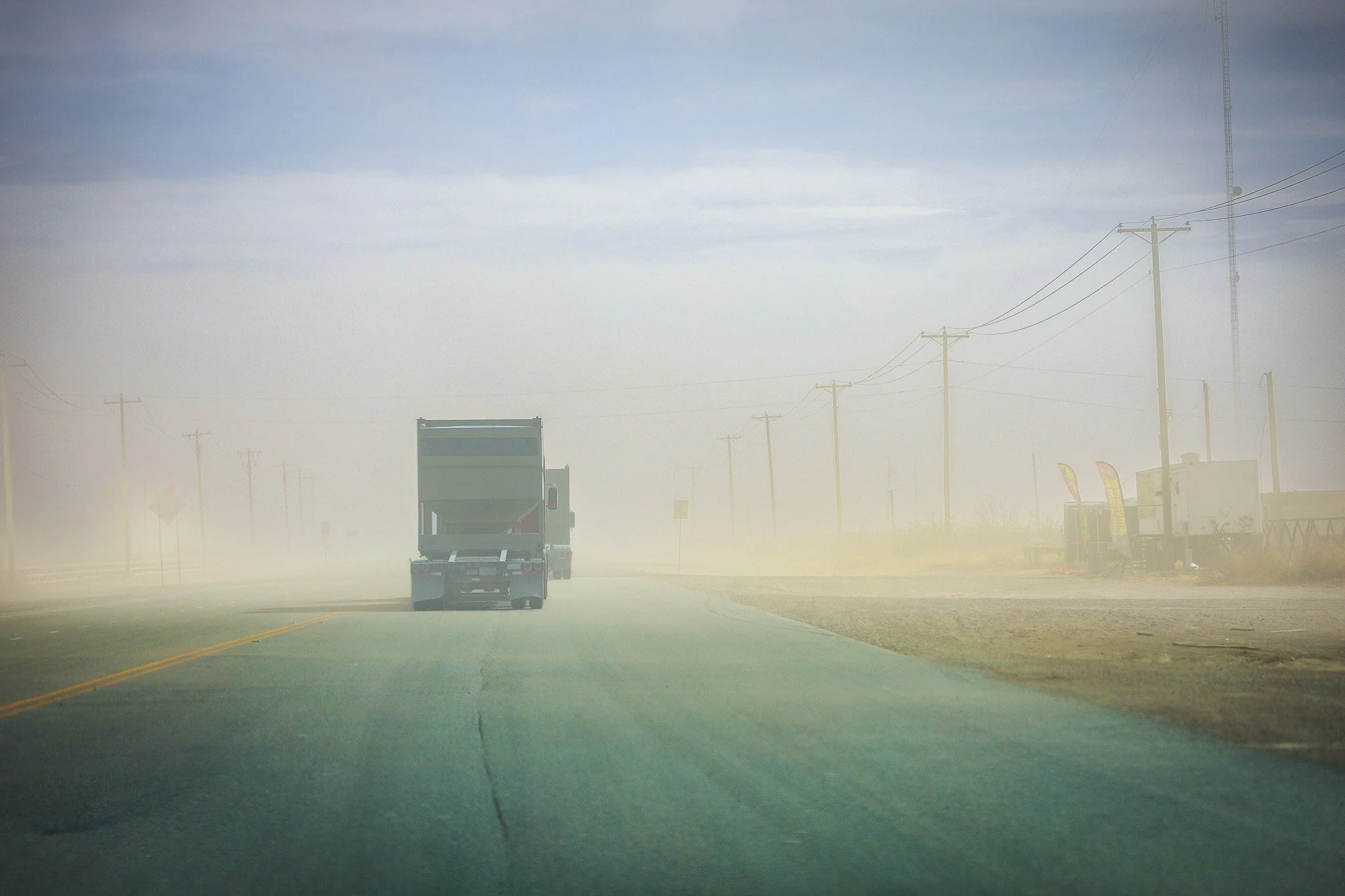 A truck driving down a foggy road, with utility poles and wires along the side, under a cloudy sky.