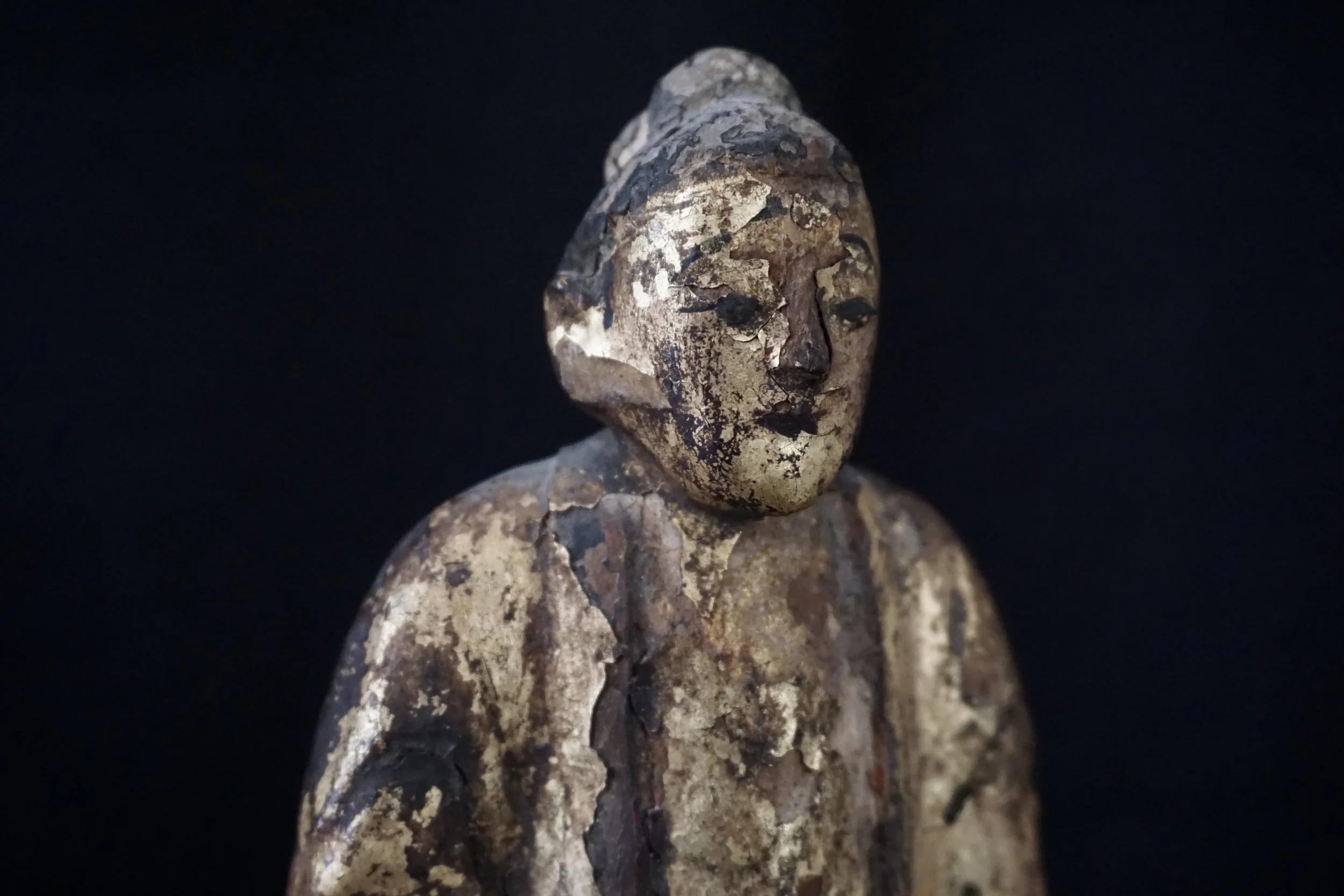 statue ancienne en bois avec visage finement sculpté, vieilli et patiné, arrière-plan noir