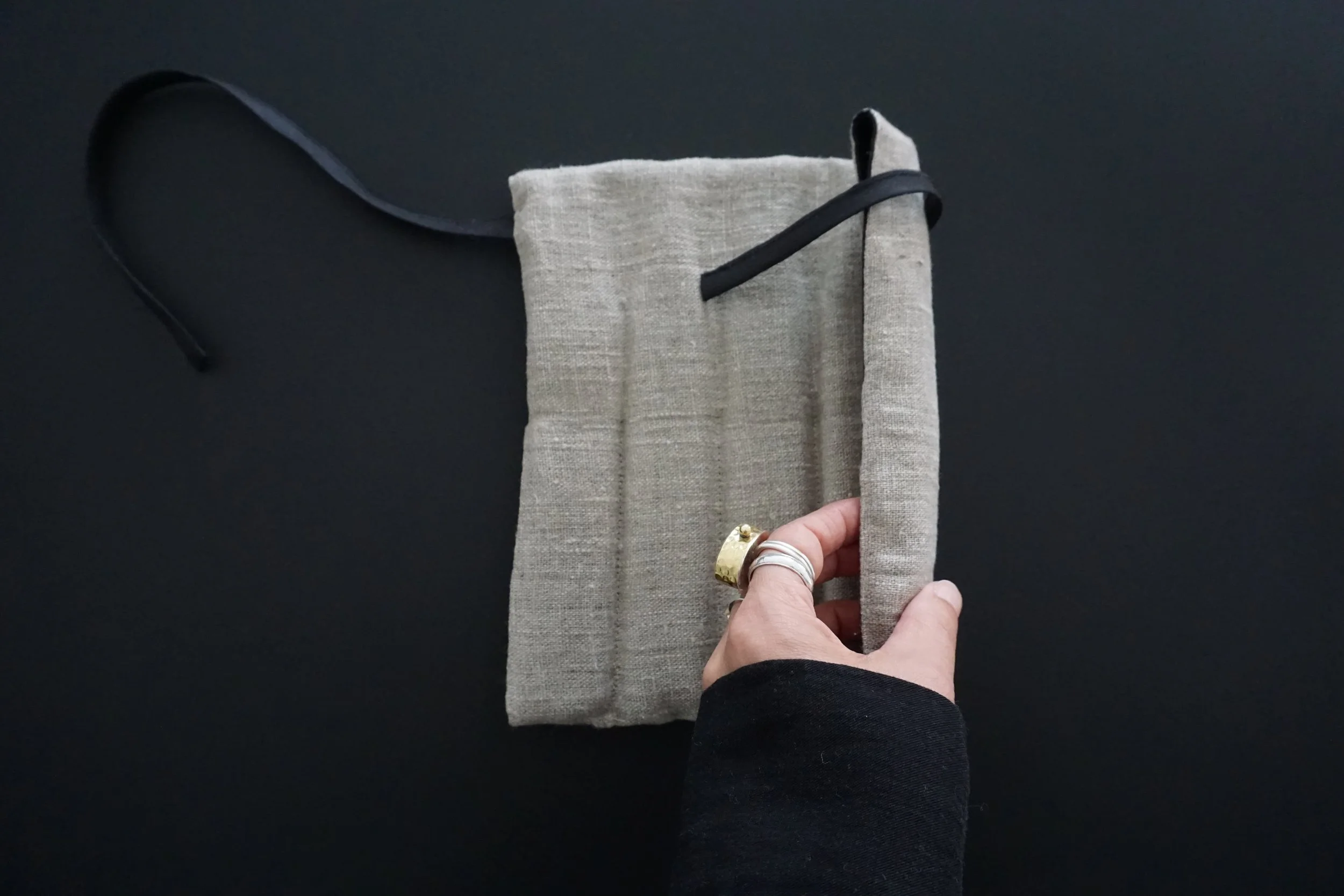 Une main tenant un petit sac en tissu beige avec une ouverture supérieure, posé sur un fond noir.