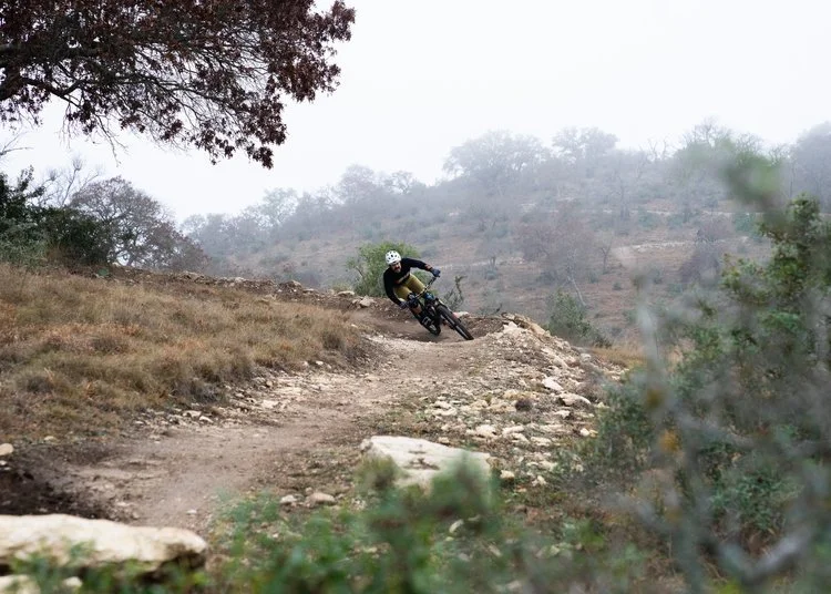 Single mountain biker coming down the trail with trees, grass, and a foggy sky