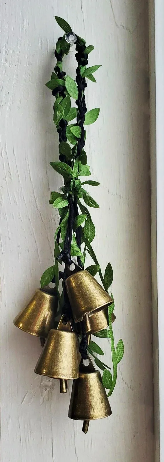 Handcrafted witch bells with brass bells, black cord, and green vine accents for doorway protection and spiritual warding