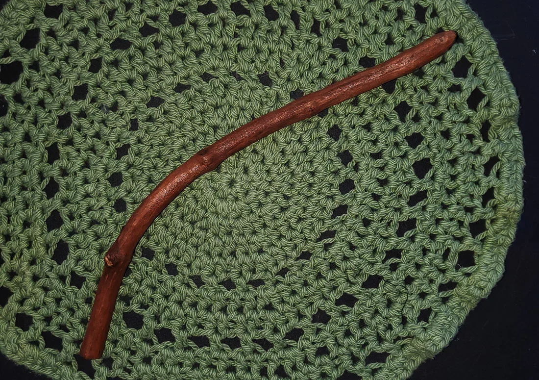 Wildwood Holler Wand #20, a curved Appalachian foraged wood ritual wand with warm natural coloring resting on a green crocheted mat.