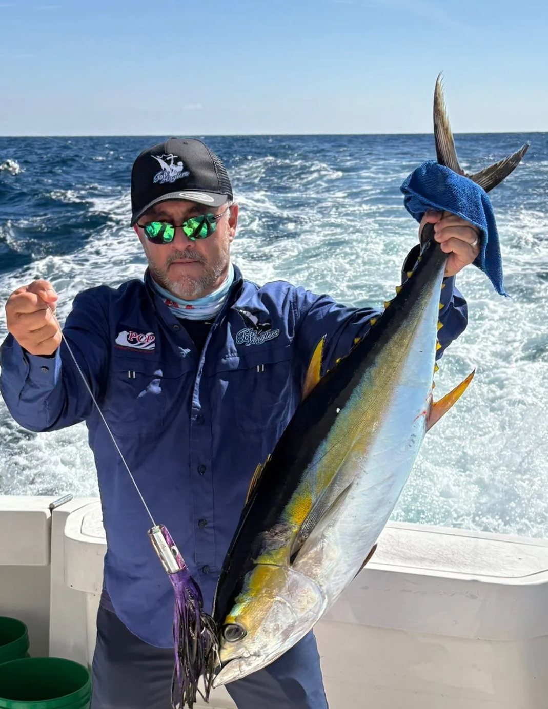 Man holding a marlinand a fishing rod on a boat in the ocean with mountains in the background Cabo San Lucas
