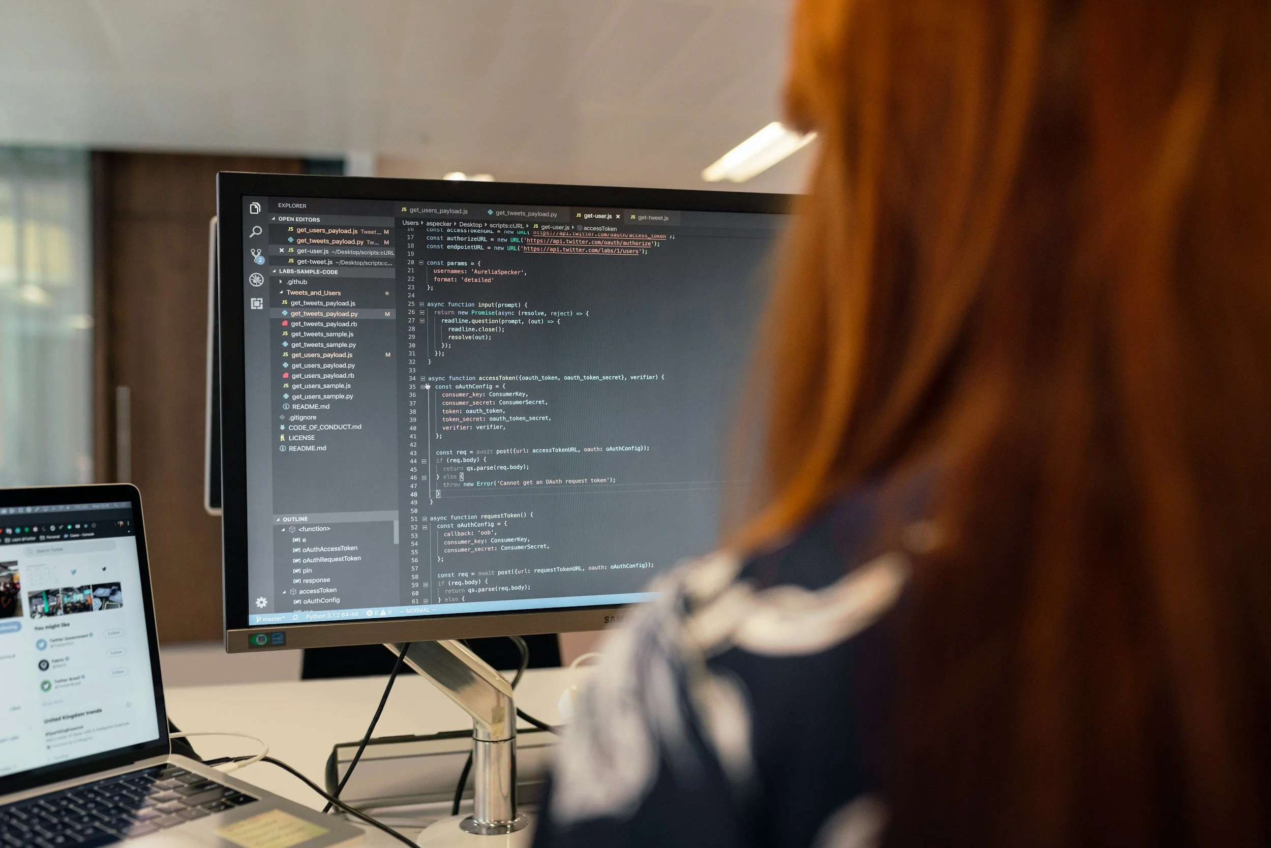 Person with reddish hair working on a computer with programming code on the monitor in an office setting.