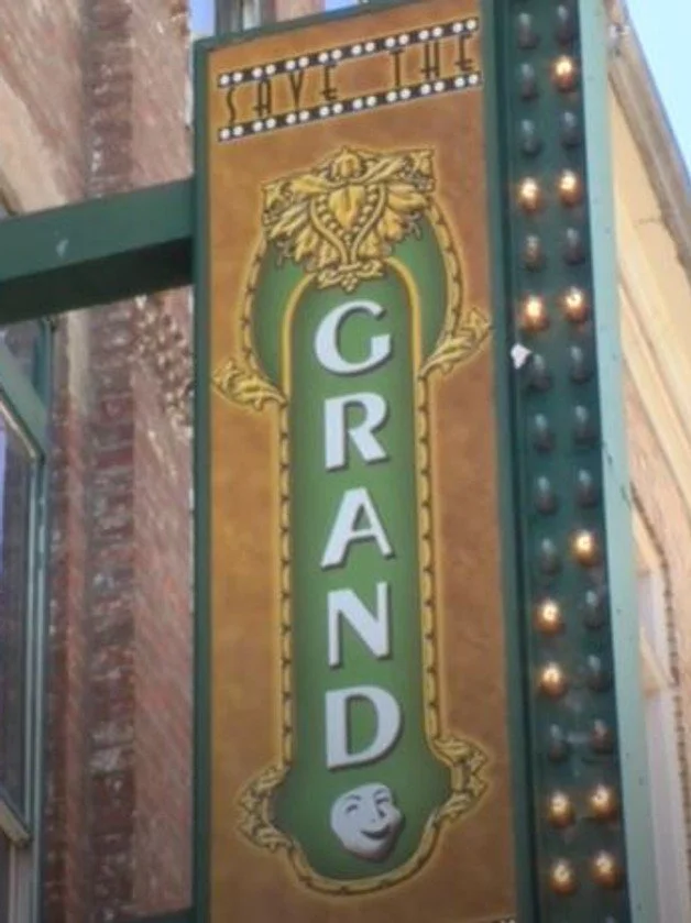 Vertical sign for the 'The Grand Theater' with a green and gold decorative border.