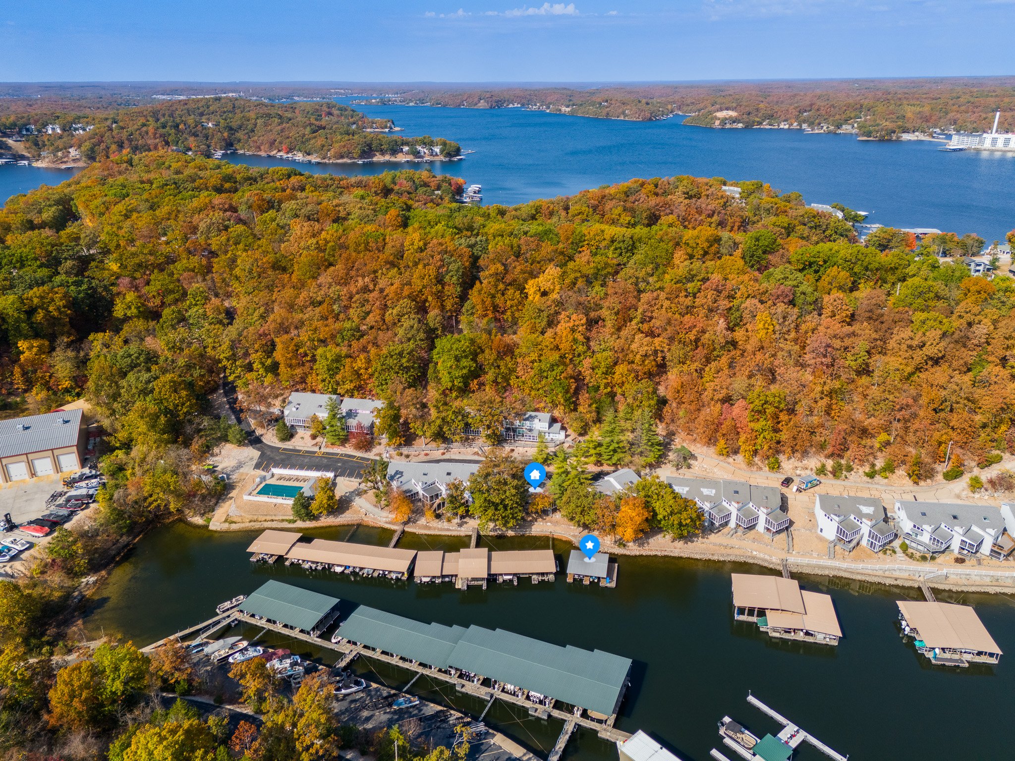 Aerial view of a lakeside landscape with docks, boats, and buildings surrounded by lush autumn foliage and a large body of water.