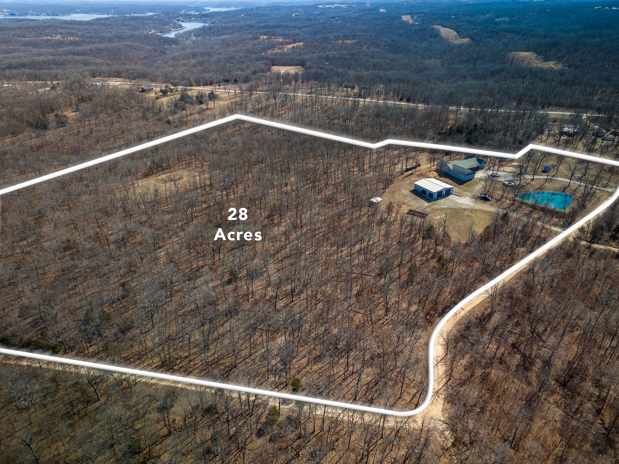 Aerial view of a 28-acre property outlined in white with buildings, a pool, and surrounding forested area.