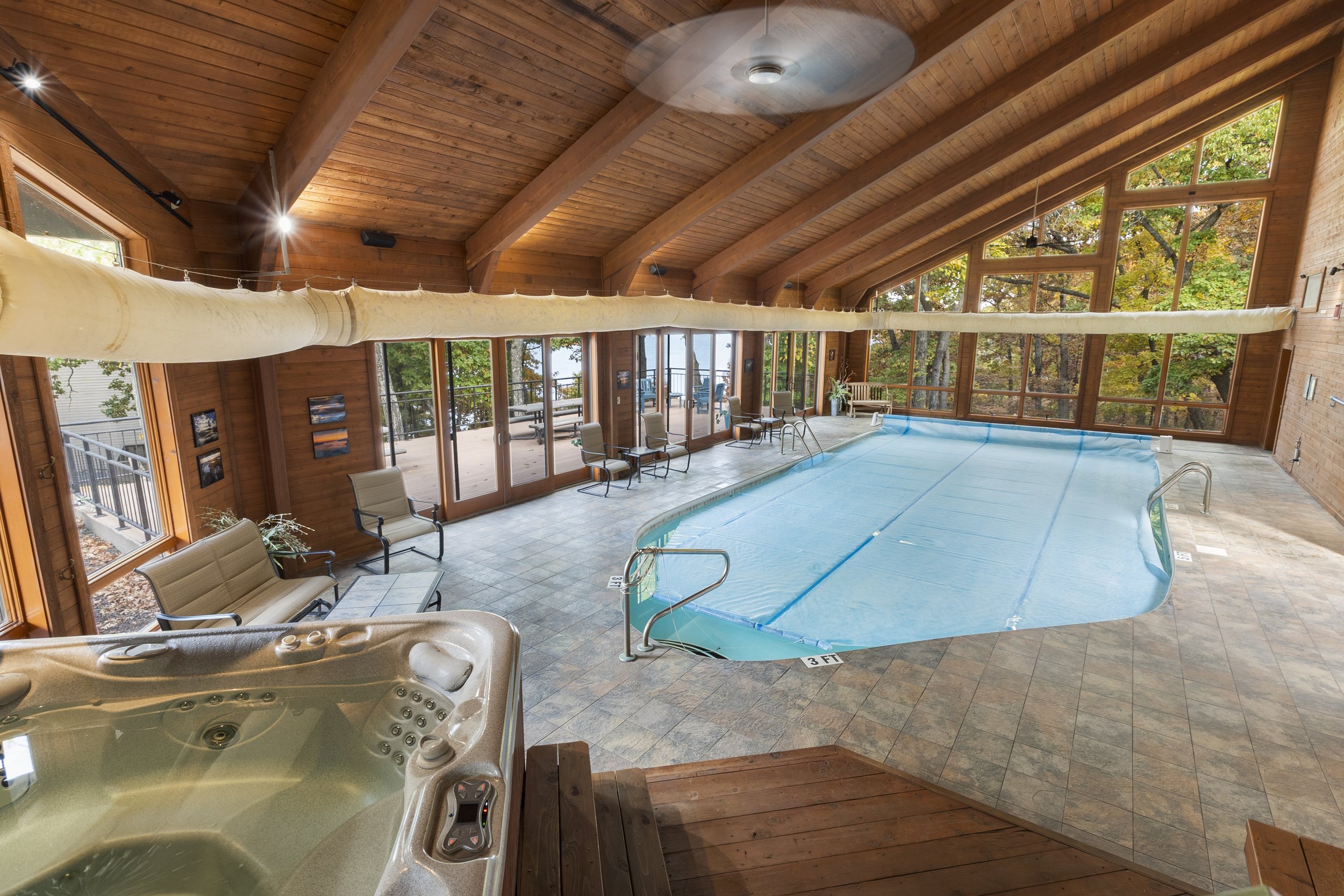 Indoor pool area with hot tub, wooden ceiling, large windows, and natural light.