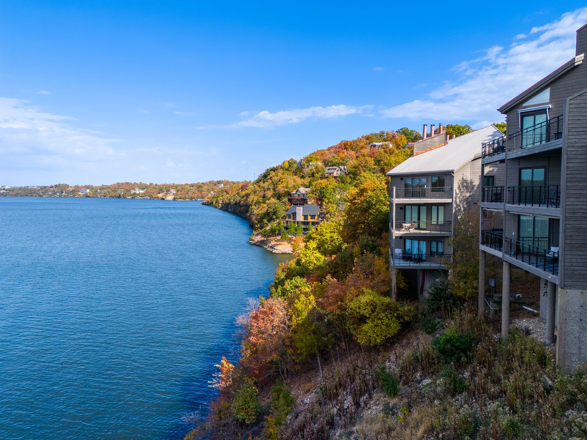 Lakeside buildings with balconies overlooking water and autumn trees.