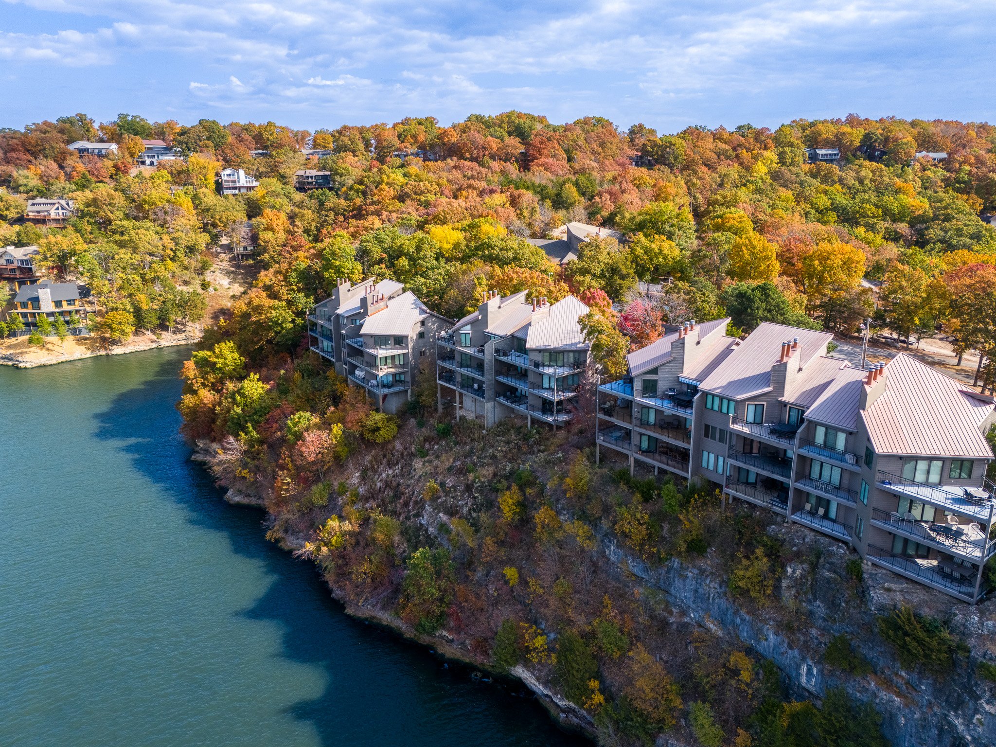 Aerial view of lakeside condos surrounded by autumn trees and adjacent to a body of water.
