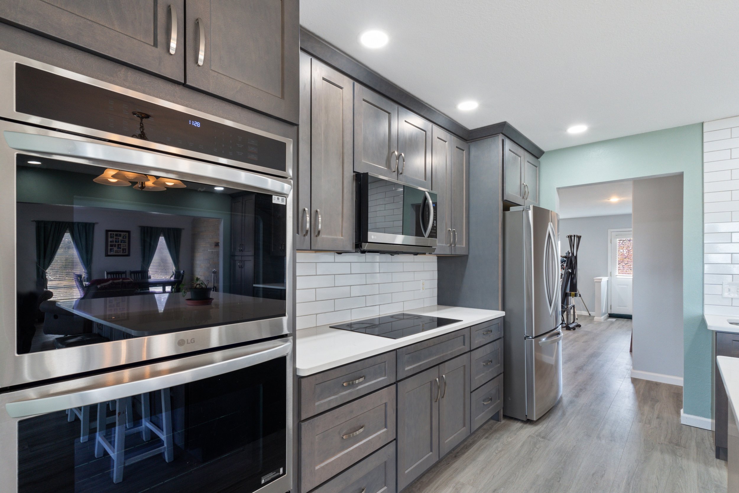 Modern kitchen with stainless steel appliances, including a double oven, microwave, and refrigerator. The space features gray cabinetry, white countertops, and a tile backsplash.