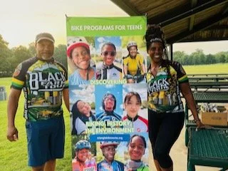 A man and a woman holding up a sign with faces of children in a youth development program.