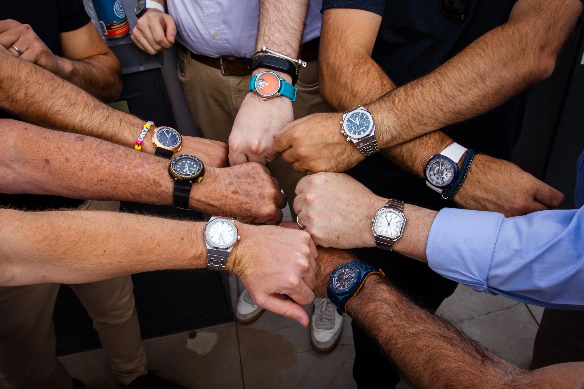 Multiple people's wrists displaying watches, joined together in a show of unity, with their fists touching in the center.
