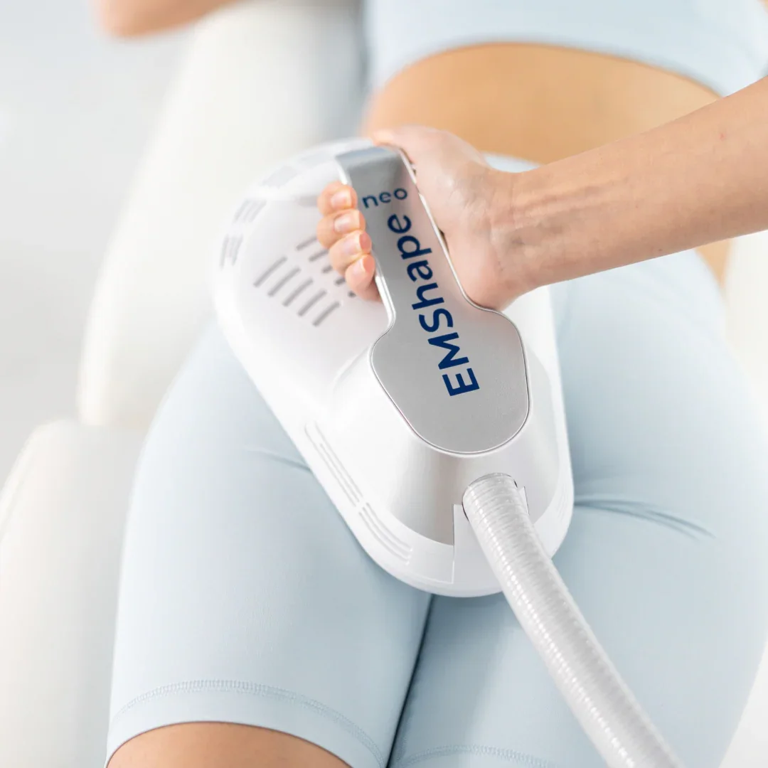 Person holding an EMShape Neo device on their thigh, wearing light-colored shorts.