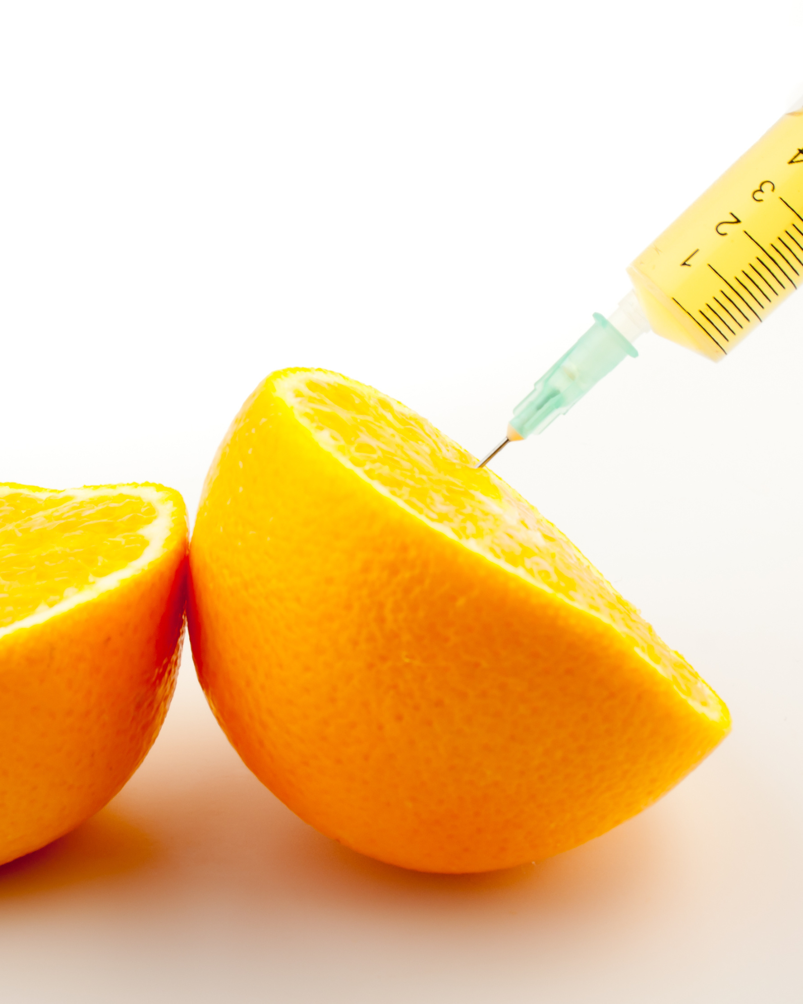 A syringe injecting into an orange that is cut in half, with another half orange beside it on a white background.
