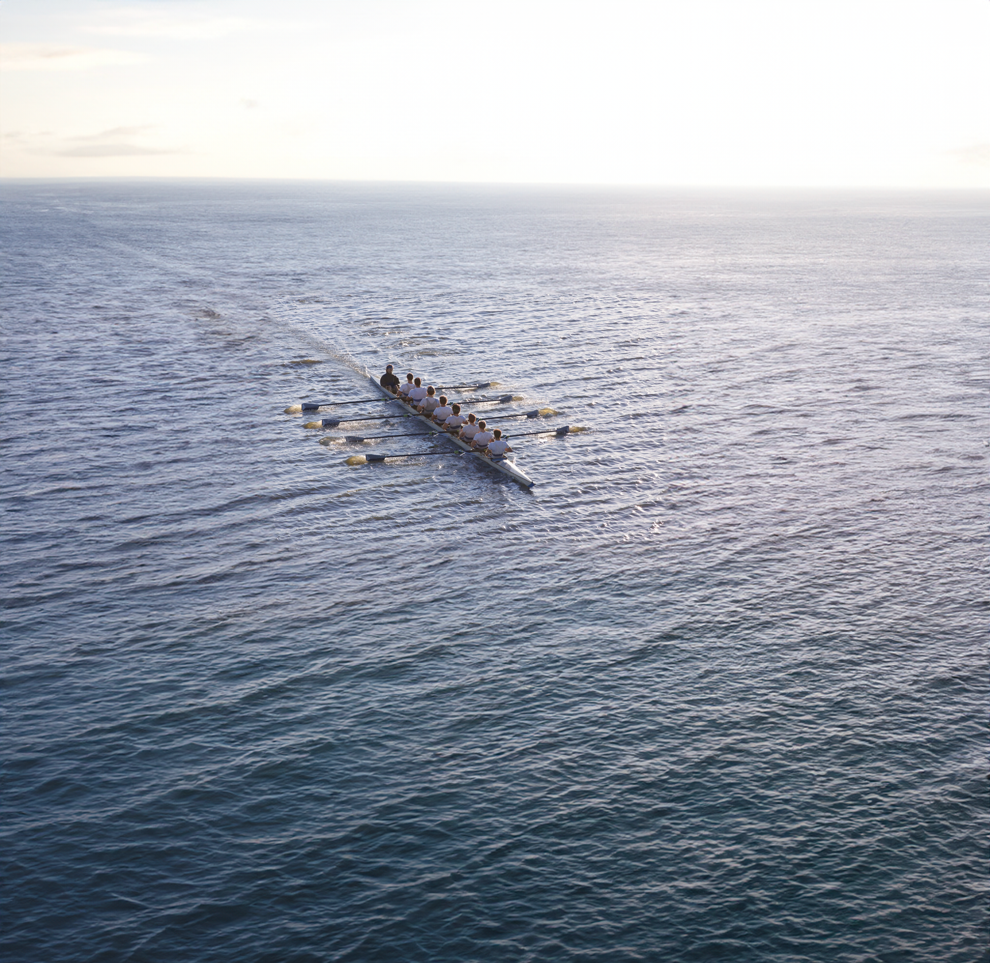 A group of people rowing a boat across a body of water during daylight, with a cloudy sky above.