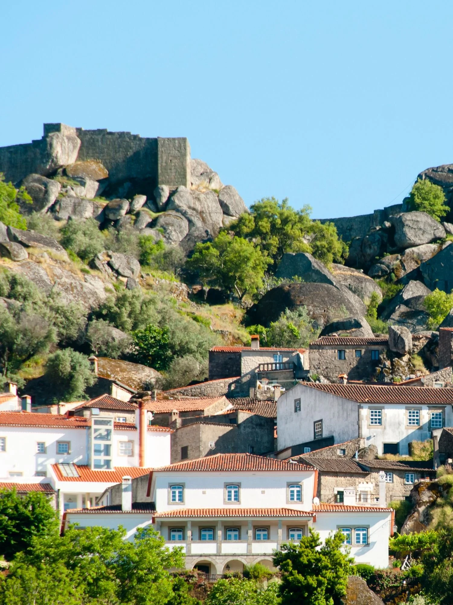 Stone houses of Monsanto village built between massive granite boulders, with a medieval castle rising above the rooftops, illustrating one of Portugal’s most distinctive historic villages set in a dramatic natural landscape.