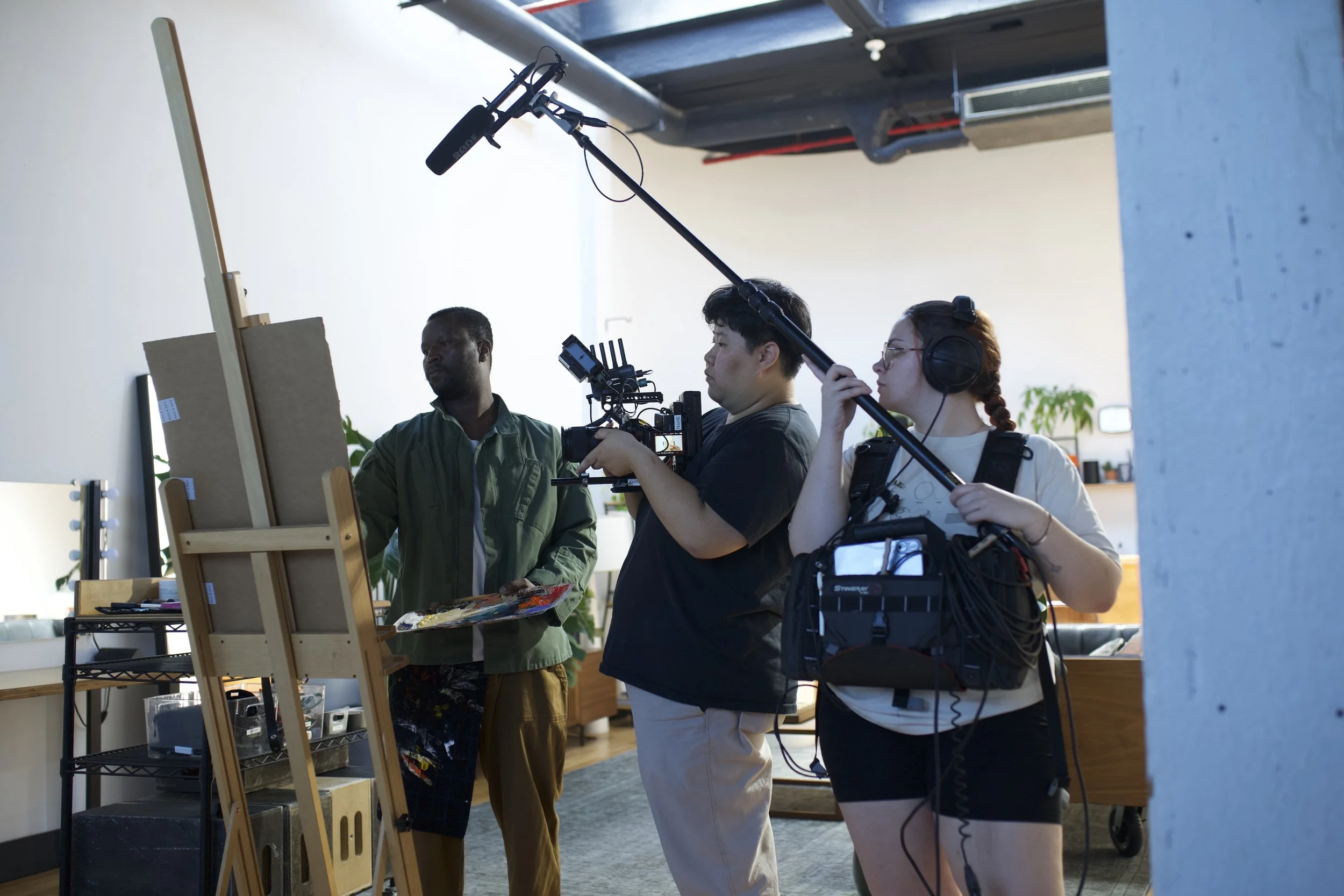 Woman on camera, woman recording audio of man painting.