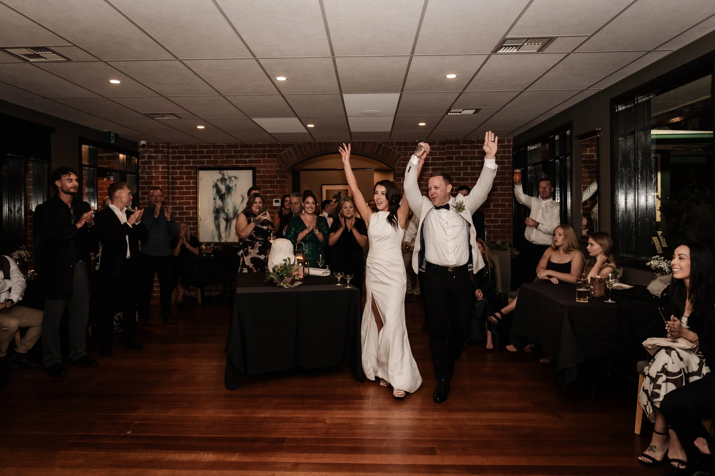 Bride and groom entering their wedding reception with arms raised to cheering guests at Jason's Restaurant Beaconsfield