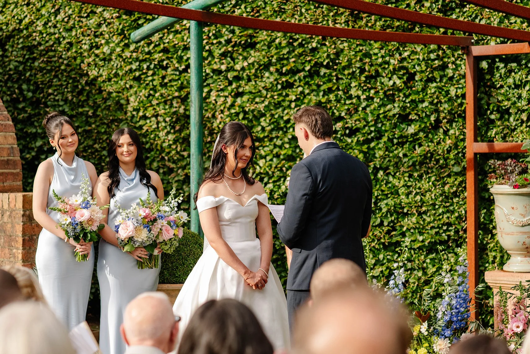 bridesmaids-bride-smile-grooms-vows-under-arbor.jpg