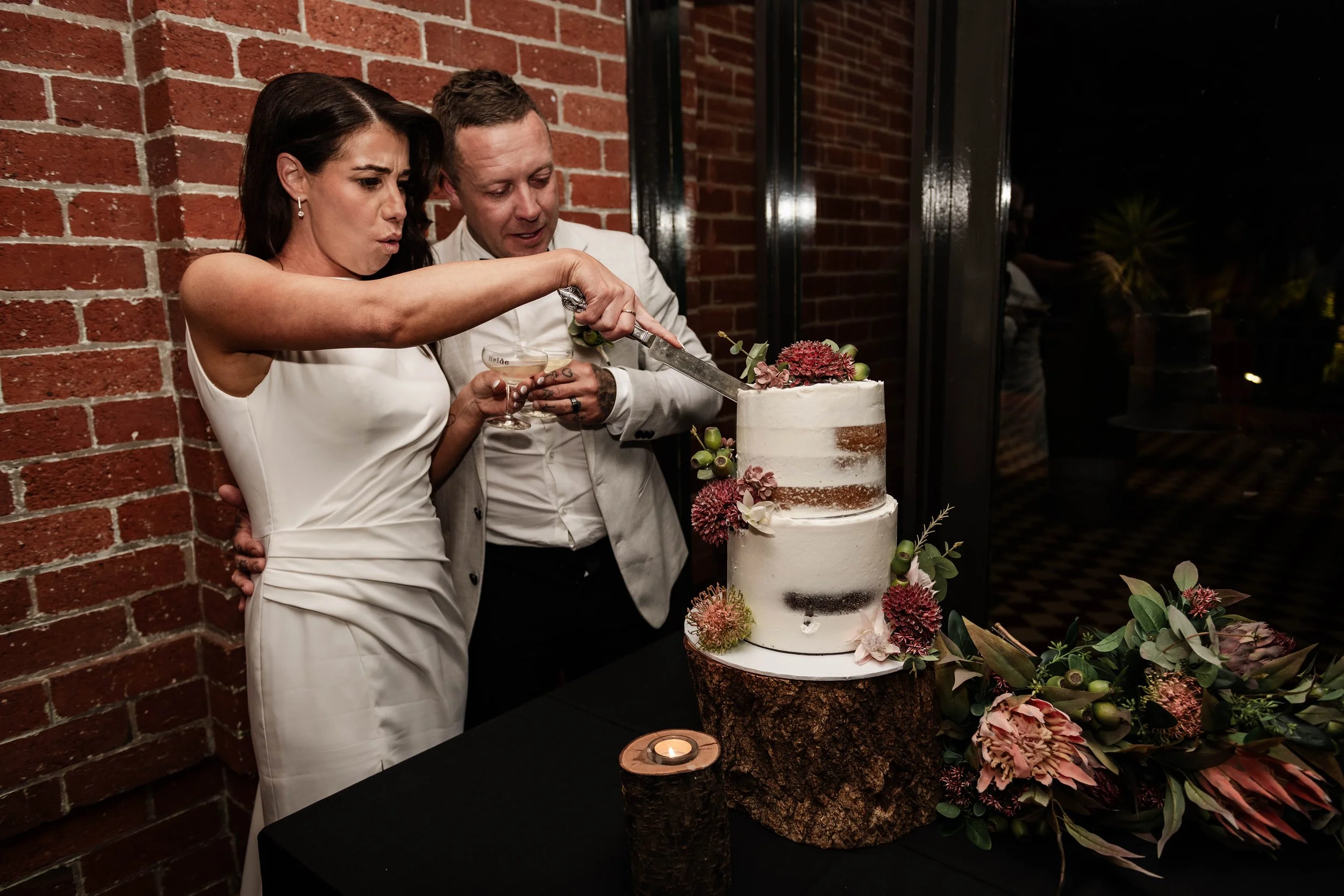Bride and groom cutting a two-tier naked wedding cake decorated with native flowers at Jason's Restaurant Beaconsfield reception