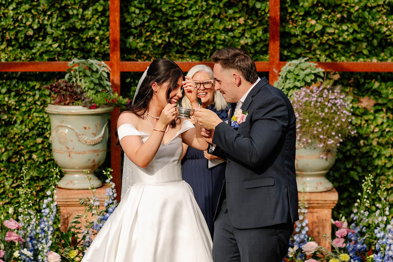 Bride and groom laughing during a wedding ceremony ritual at Cloudehill Gardens Dandenong Ranges with celebrant and floral backdrop