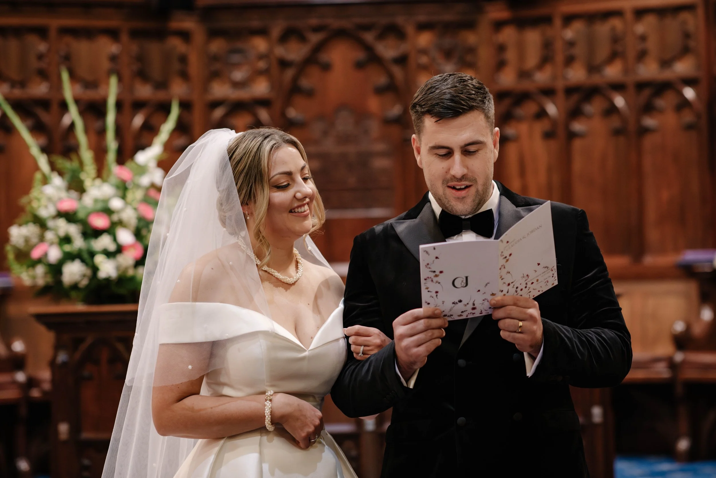 bride and groom stand together as they smile and they read from their church service