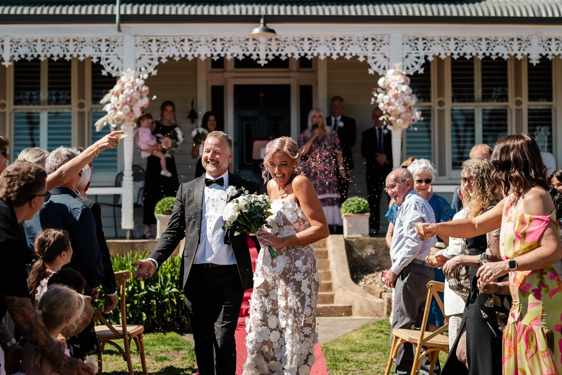 Newly married couple walking down the aisle as wedding guests toss confetti outside a historic-style wedding venue