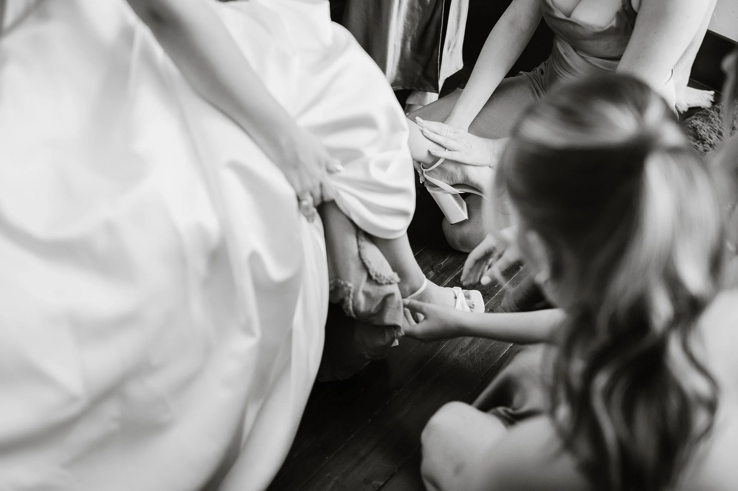 Closeup of bridesmaids helping bride put shoes on black and white