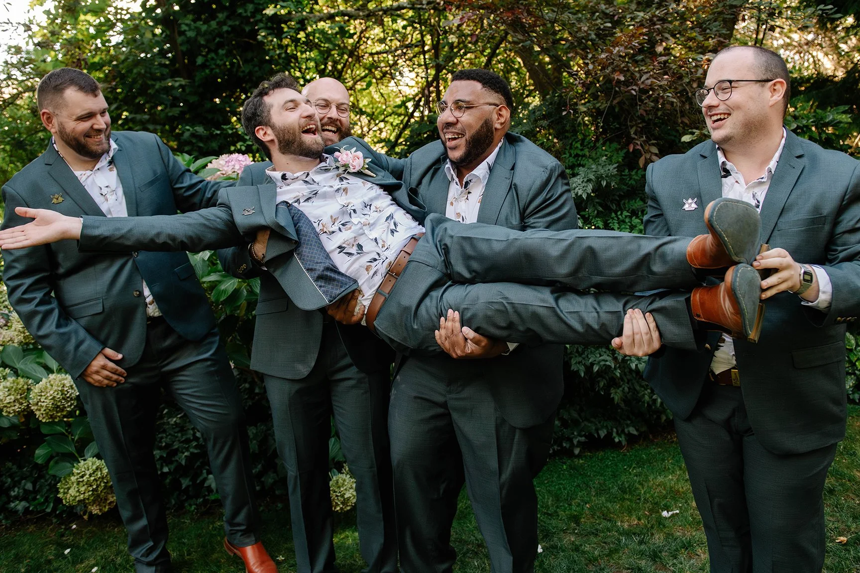 groomsmen hold groom in air vertically as they all laugh and smile in green Chateau Dore garden Bendigo