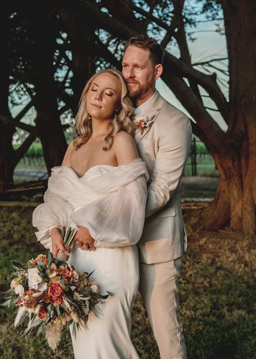 Bride and groom embracing at sunset among gnarled trees at Barn and Co wedding venue Victoria