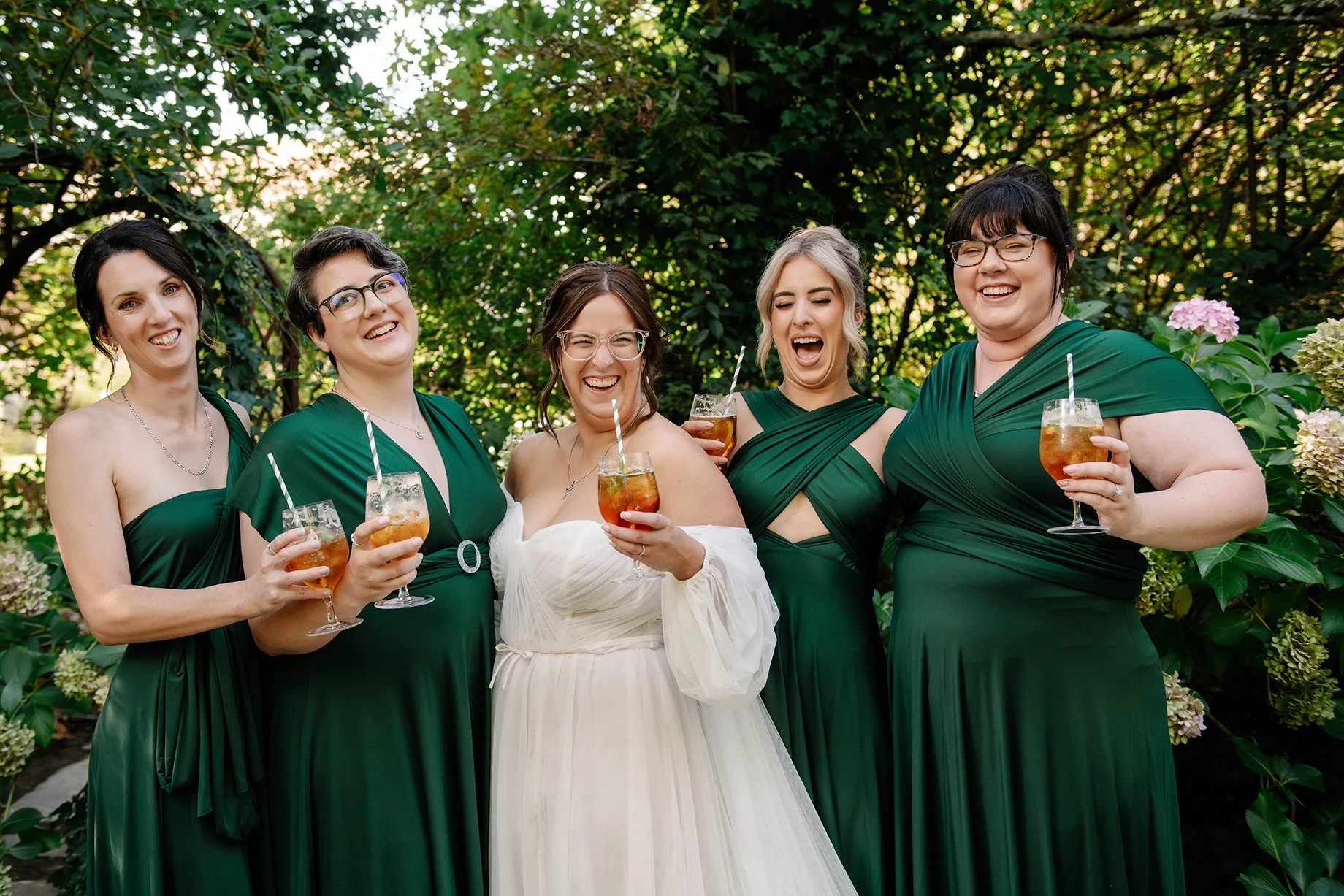 bride smiling posed photo with bridesmaid in green dresses holding orange drinks in Bendigo