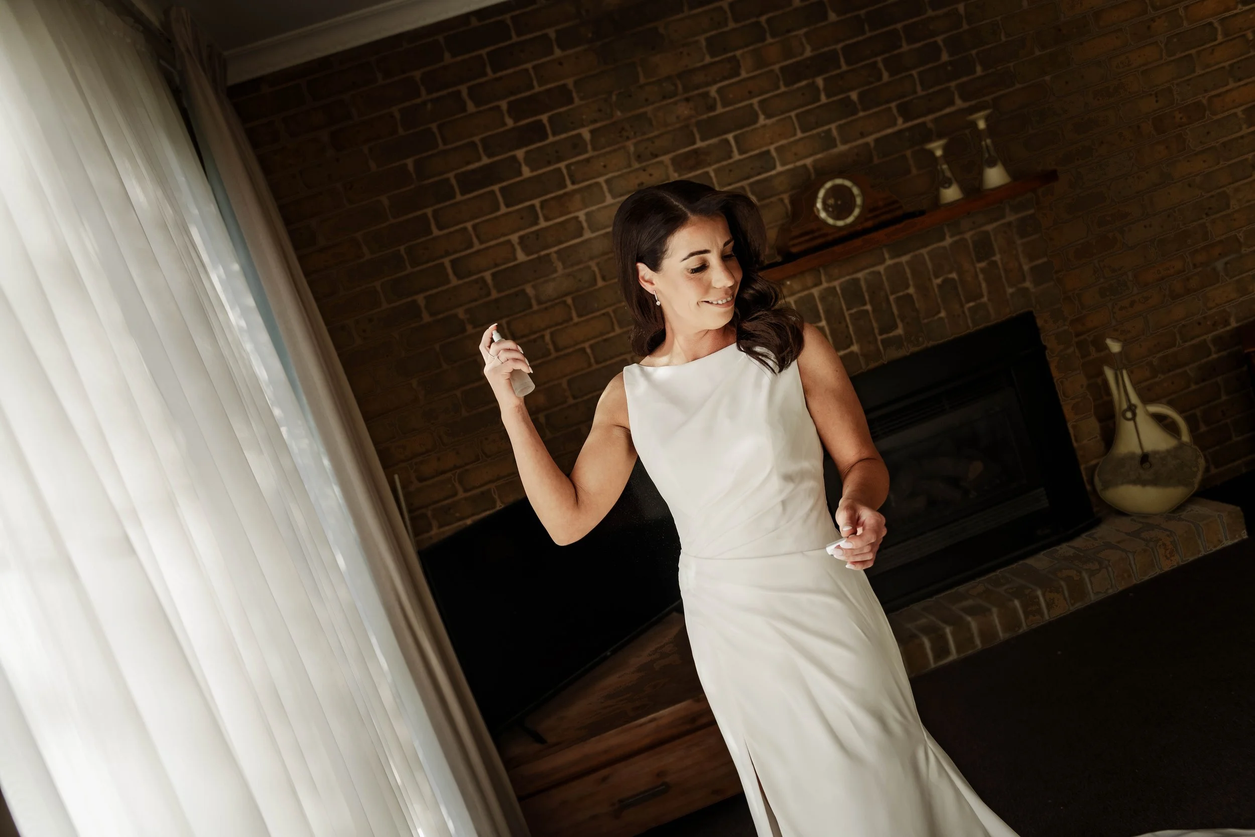 Bride spraying perfume while getting ready in a brick-walled room at Jason's Restaurant Beaconsfield Victoria